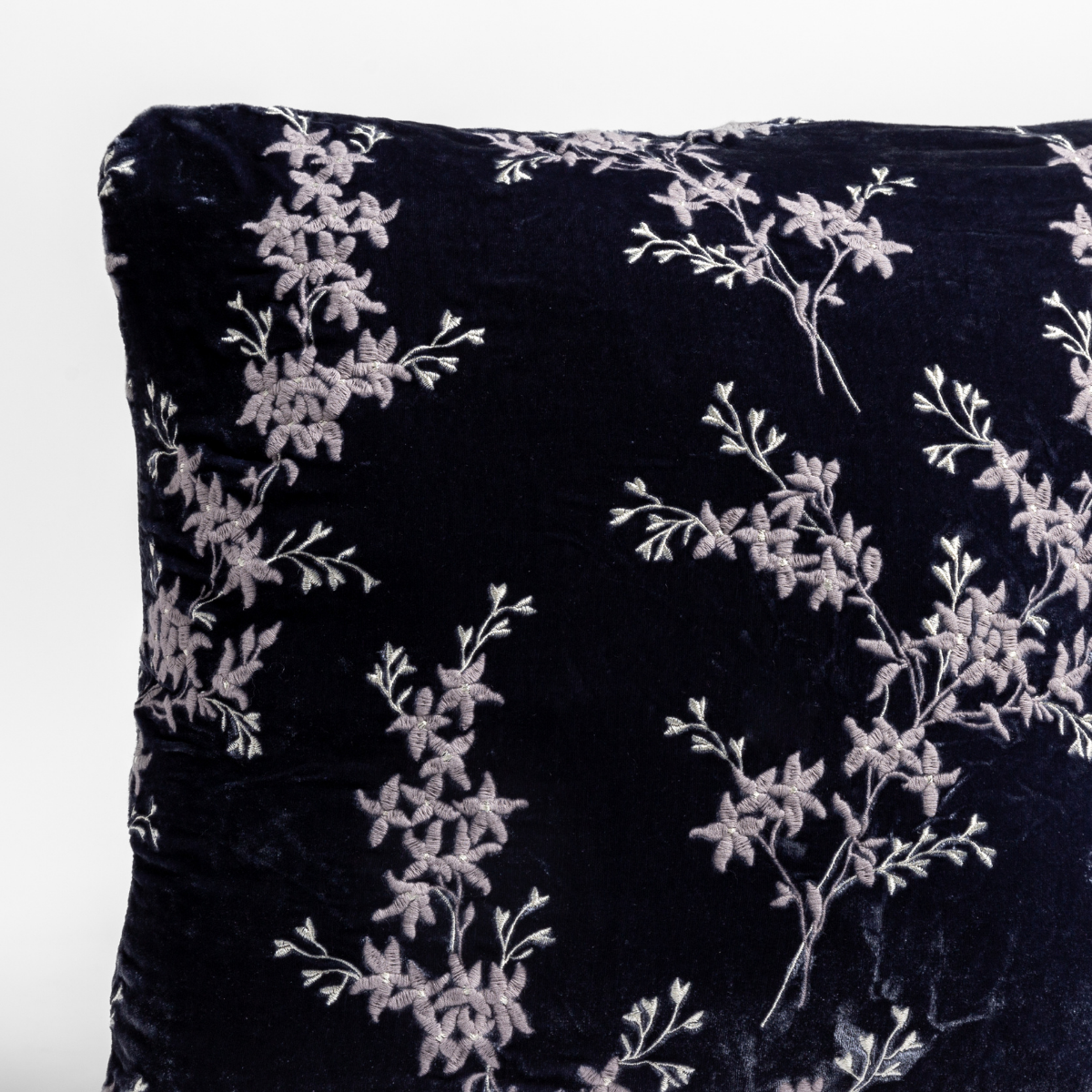 Close up of the corner of a floral embroidery patterned silk velvet pillow cushion in french lavender, a purple tone. 
