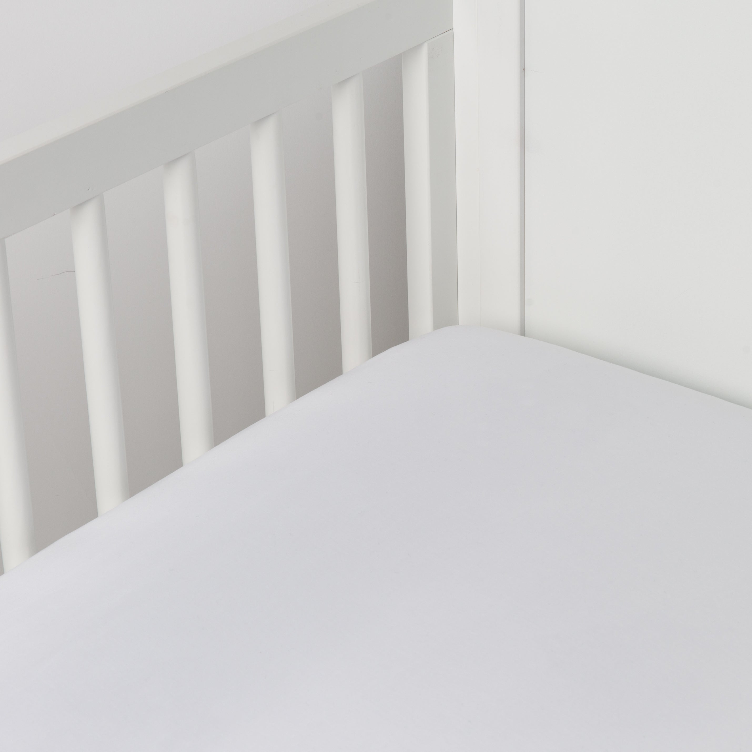 White: crib sheet shown on a mattress shown from overhead into the corner of a crib. 