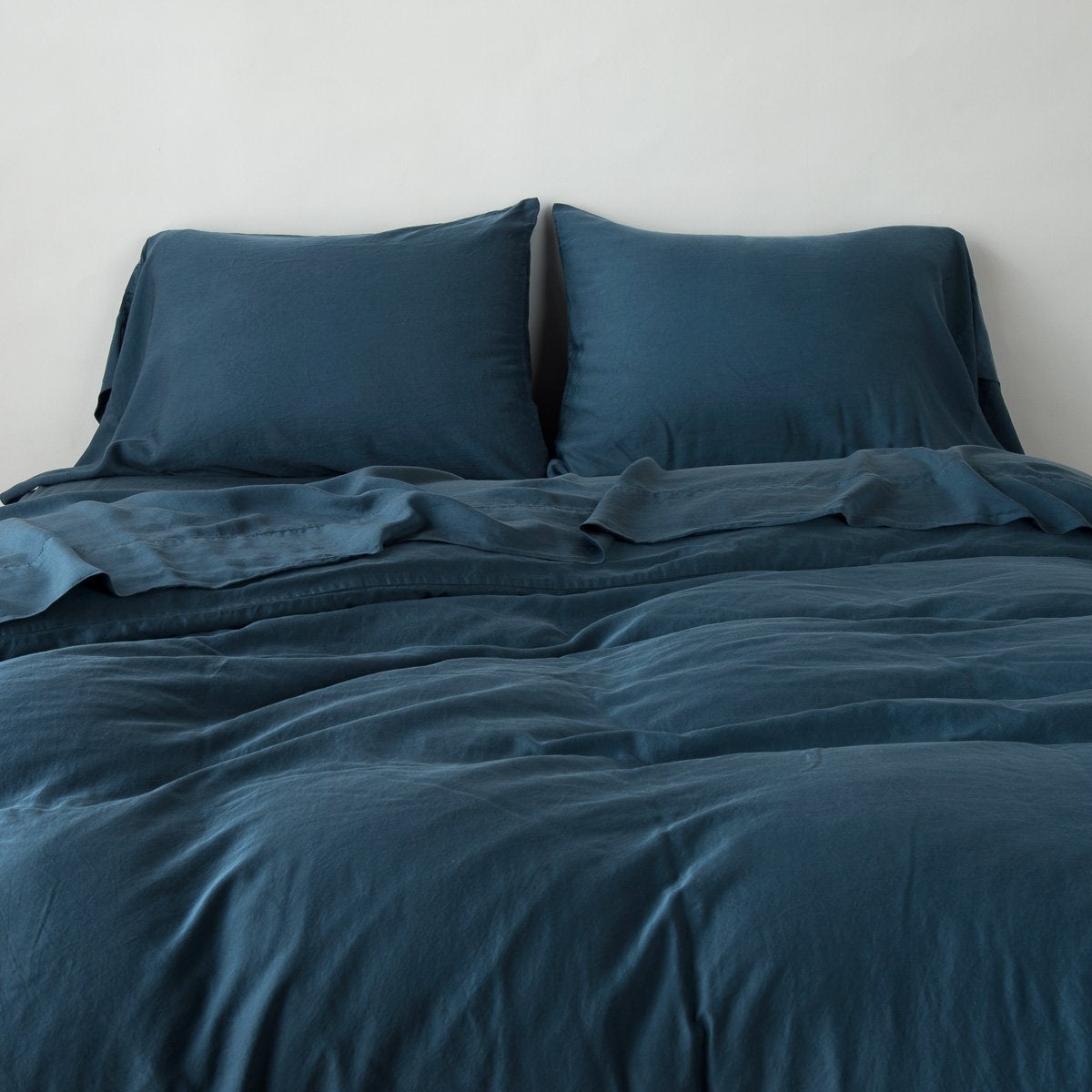 Midnight: duvet cover with matching sleeping pillows and sheeting against a white wall - end of bed view.