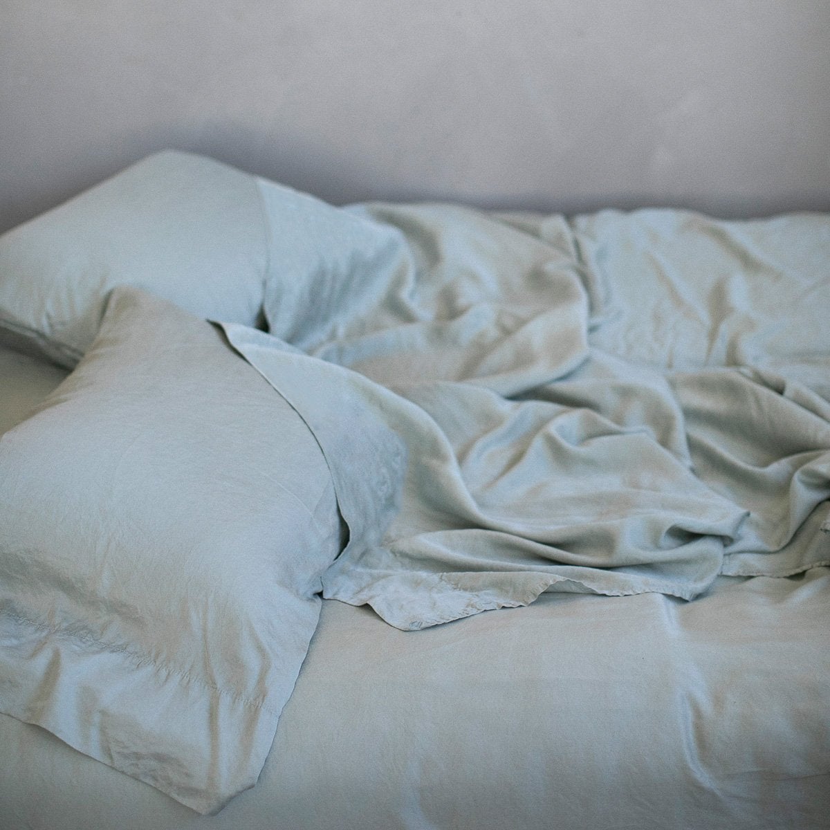 : Rumpled Madera Luxe sleeping pillows and matching sheeting - mineral, slightly overhead side view.