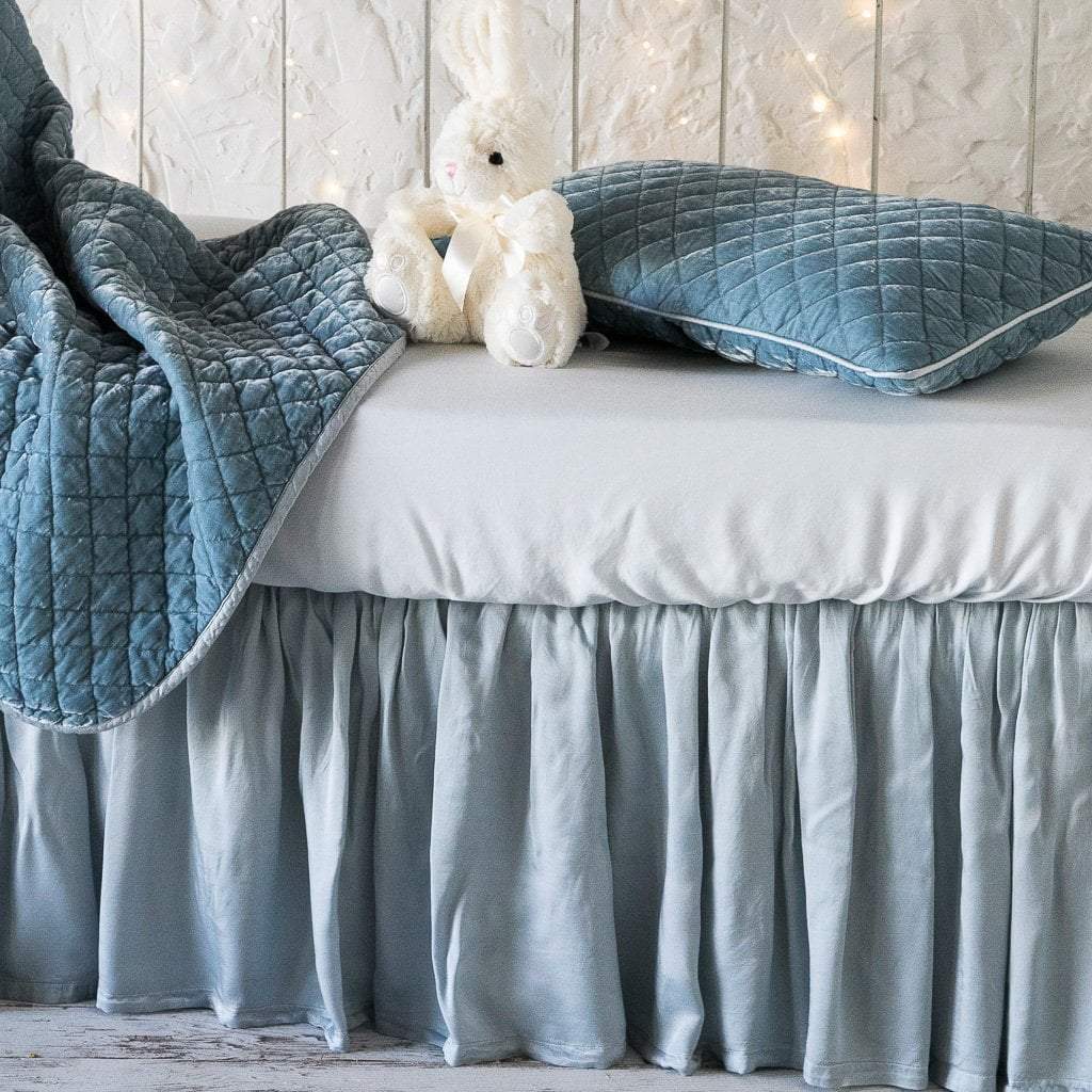 : Madera Luxe crib sheet shown on a white iron crib with silk velvet throw blanket and pillow, all in cloud - side view.