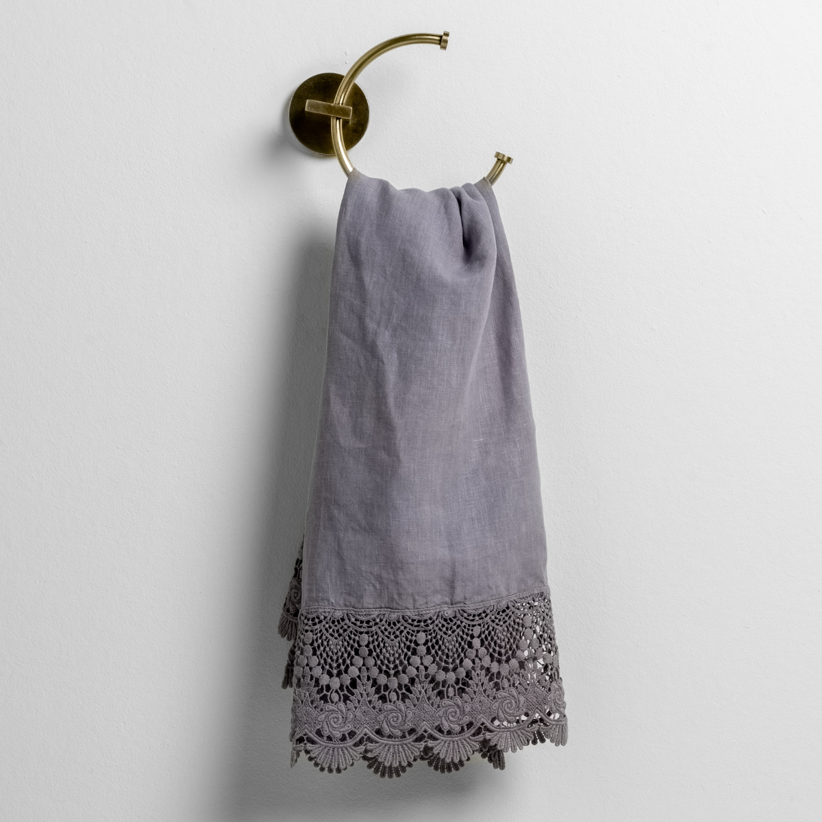 French Lavender: linen with mattine lace trimmed guest towel on a decorative towel ring mounted on a white wall. 