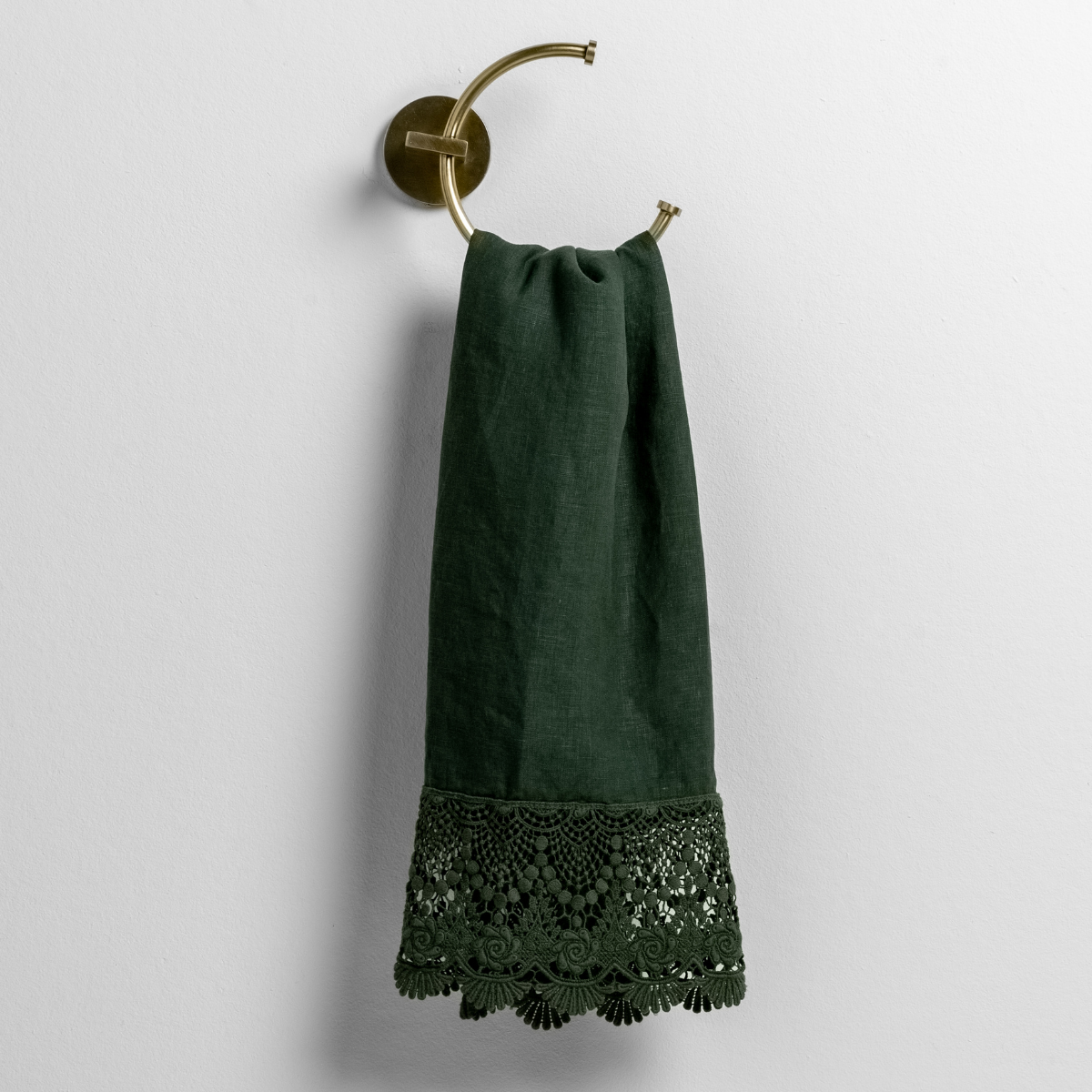Juniper: linen with mattine lace trimmed guest towel on a decorative towel ring mounted on a white wall. 