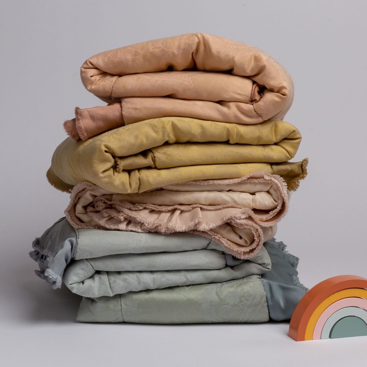: a stack of silk and tencel™ baby blankets shown in pastel rainbow colors with  a set of toy blocks as a rainbow. 