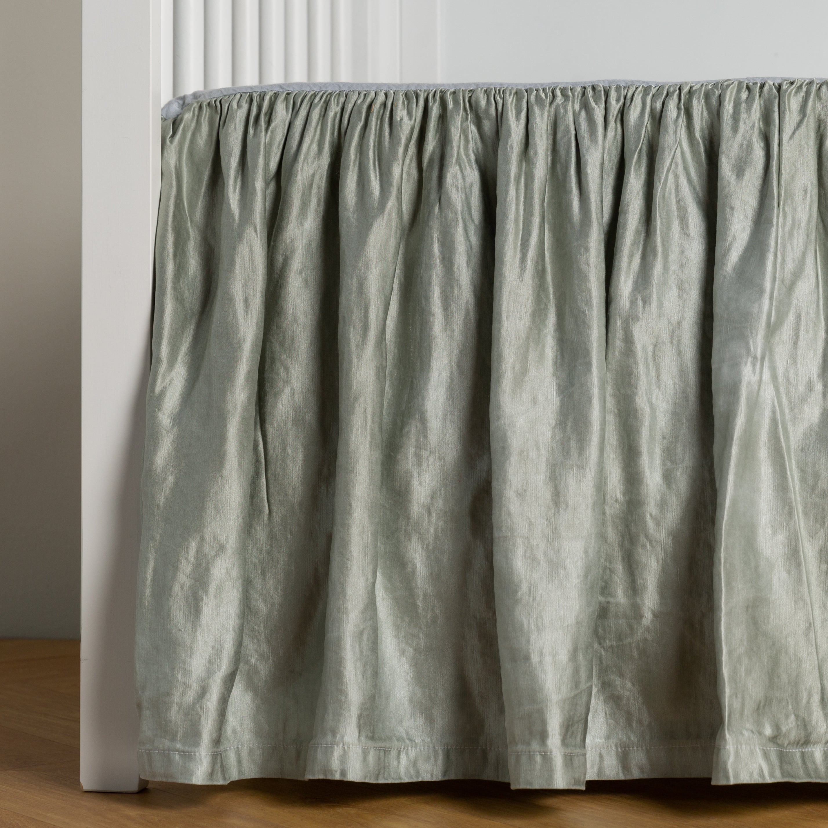 Mineral: charmeuse crib skirt shown on a white crib against a white wall and medium wood floor. 