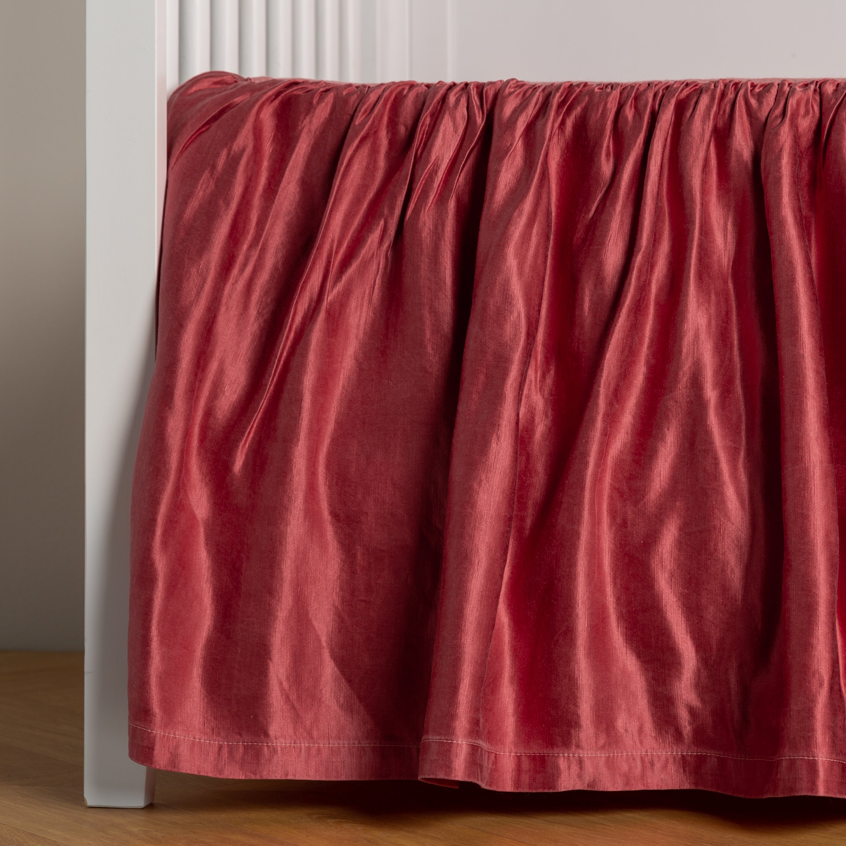Poppy:  charmeuse crib skirt shown on a white crib against a white wall and medium wood floor. 