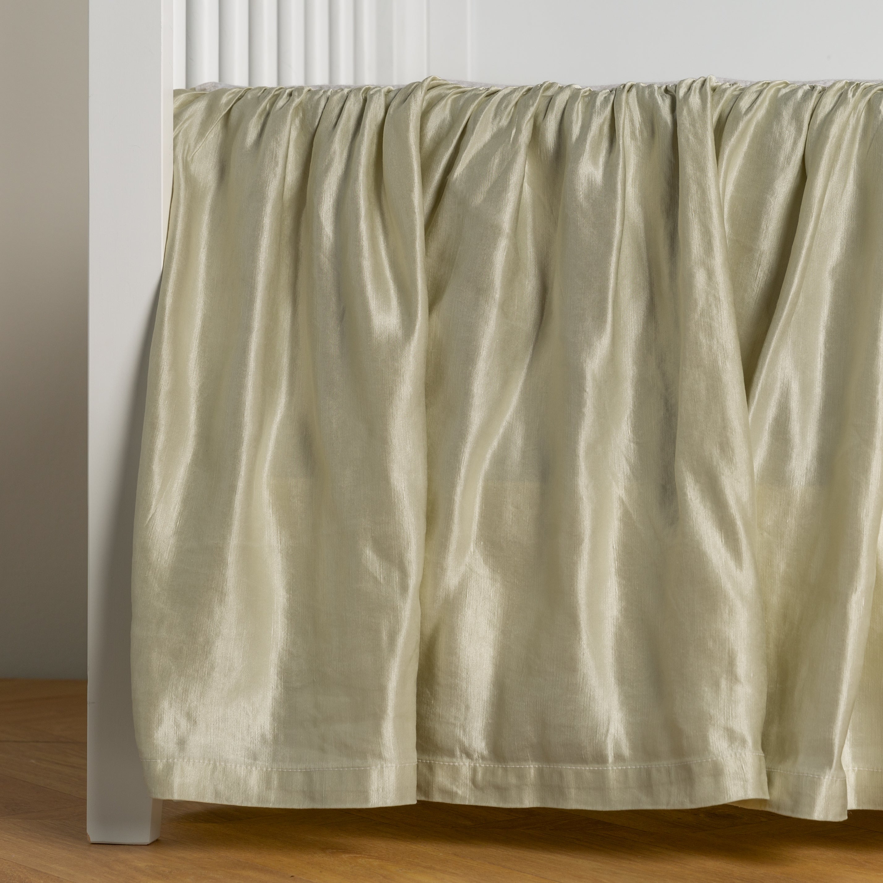 Parchment:  charmeuse crib skirt shown on a white crib against a white wall and medium wood floor. 
