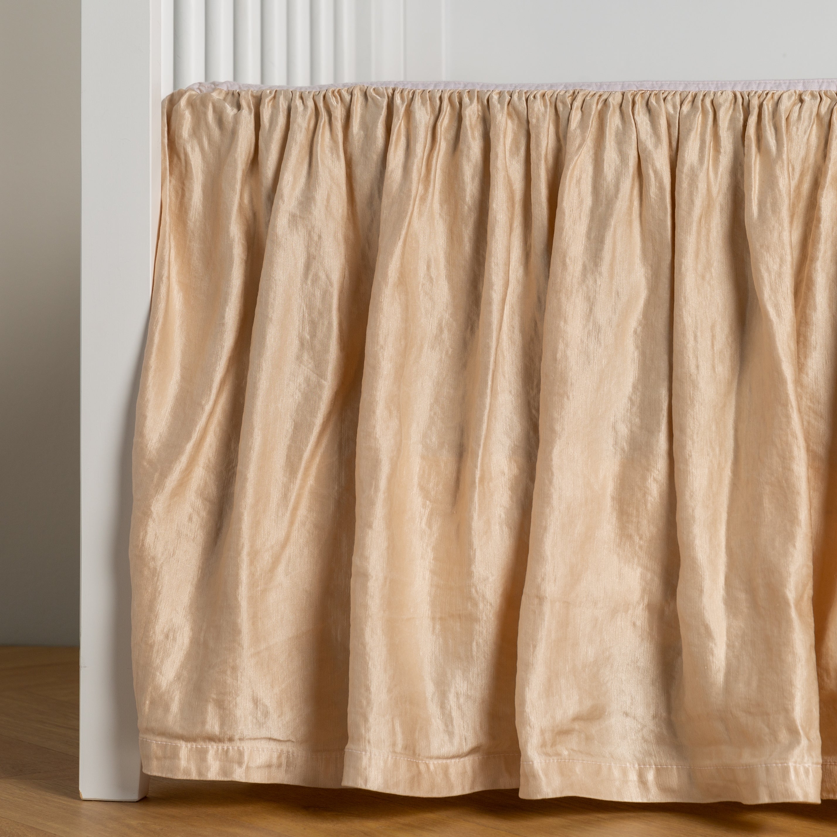 Pearl:  charmeuse crib skirt shown on a white crib against a white wall and medium wood floor. 