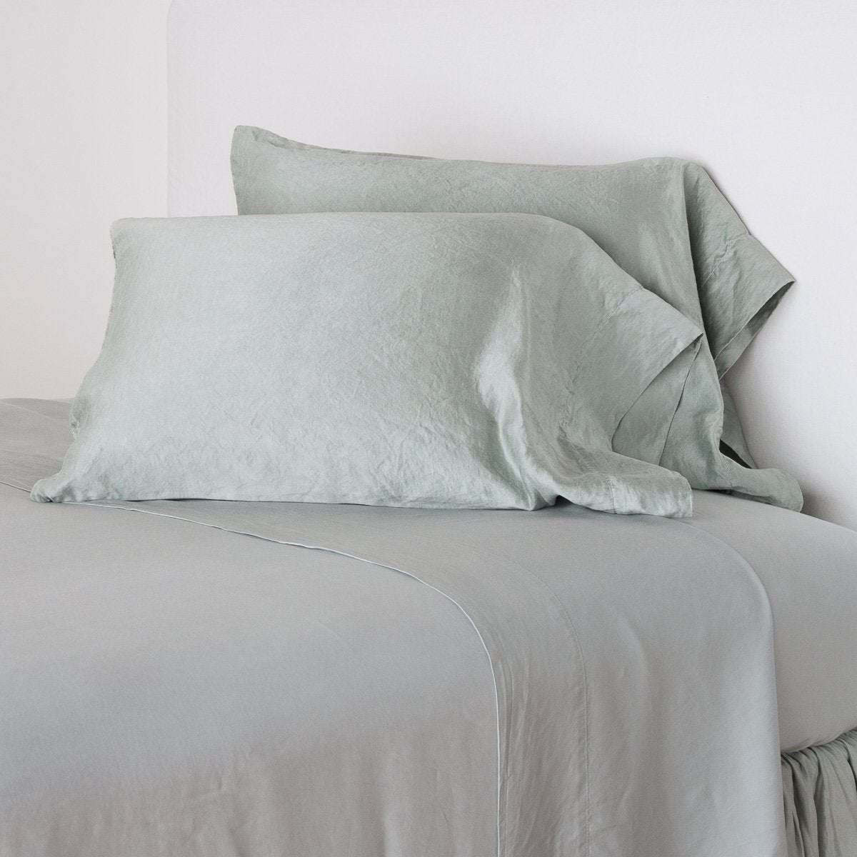 : Paloma sleeping pillows leaning upright against a white wall on monochromatic sheeting - eucalyptus, cropped three-quarter angle.