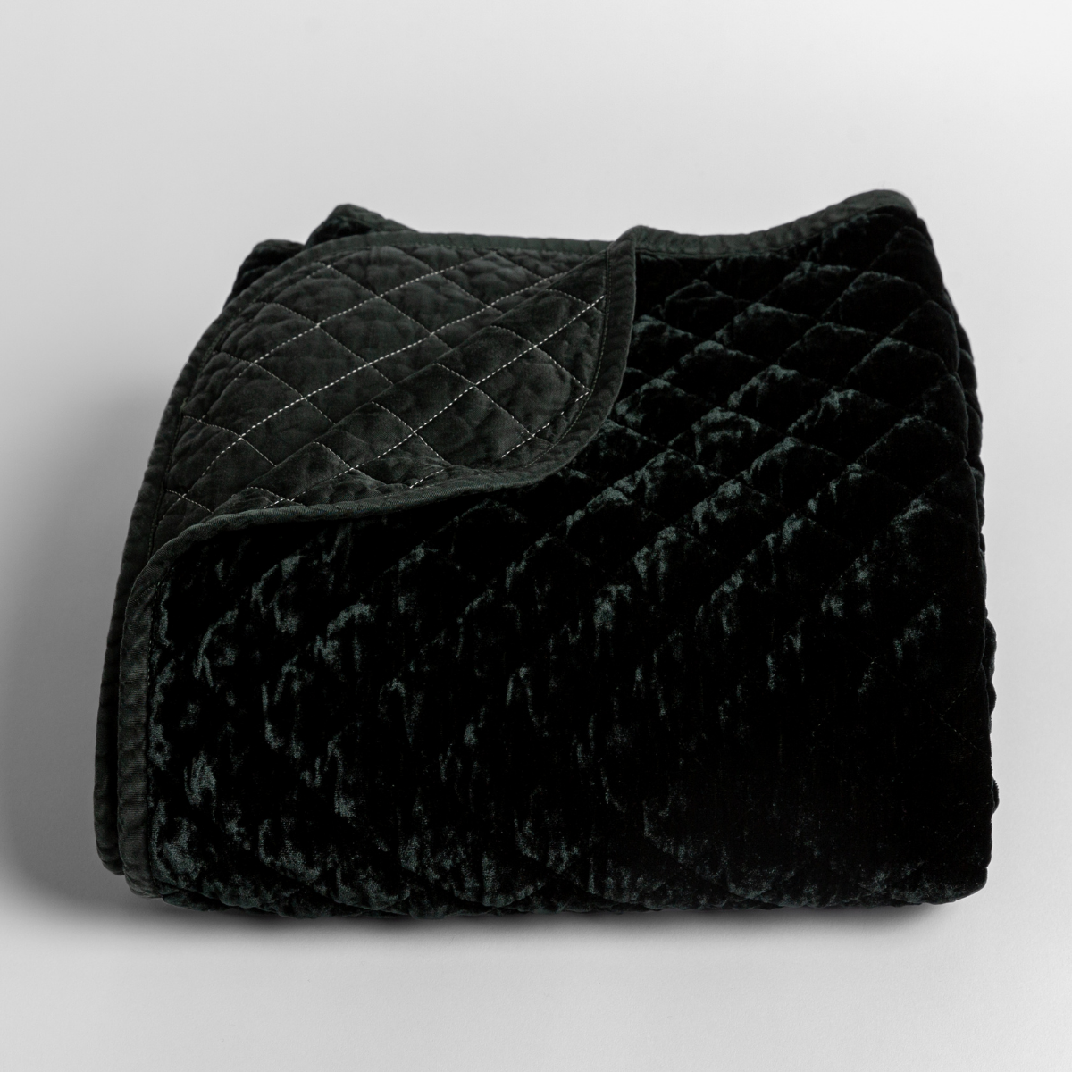 Juniper: quilted silk velvet quilted blanket folded with a corner folded back to reveal its satin back and binding. 