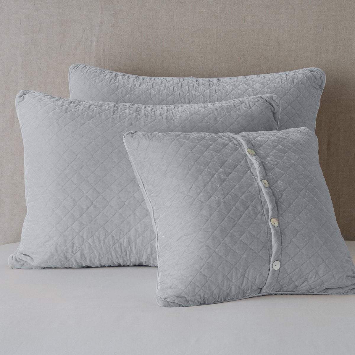 Sterling: shams leaning upright against a neutral headboard. One sham is backwards to showcase the shimmering shell button closure.