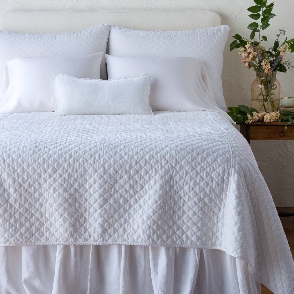 White: : shams with matching coverlet on a neatly-made, monochromatic bed - end of bed view.