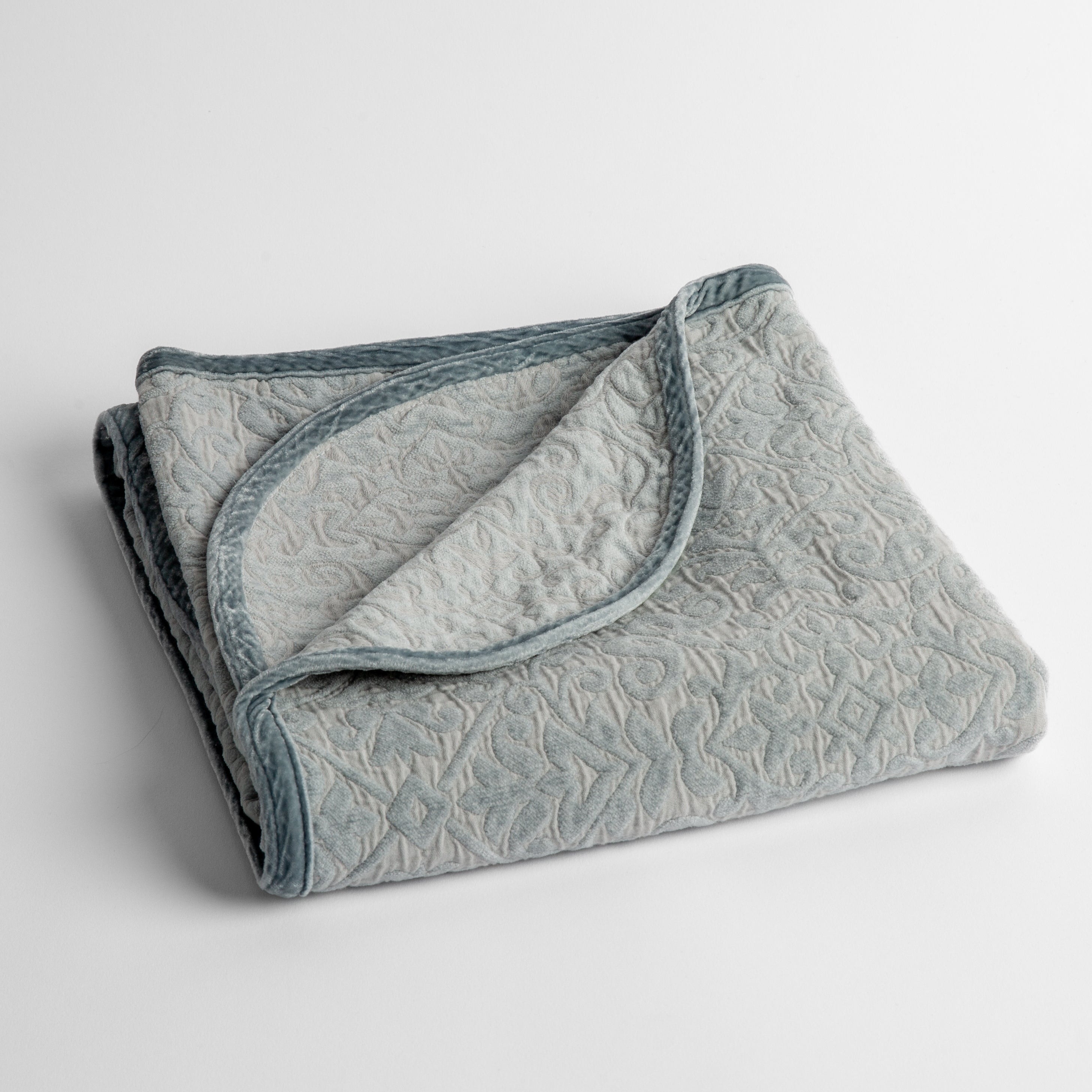 Cloud: a folded cotton chenille baby blanket trimmed in silk velvet shot overhead at a slight angle against a white background. 