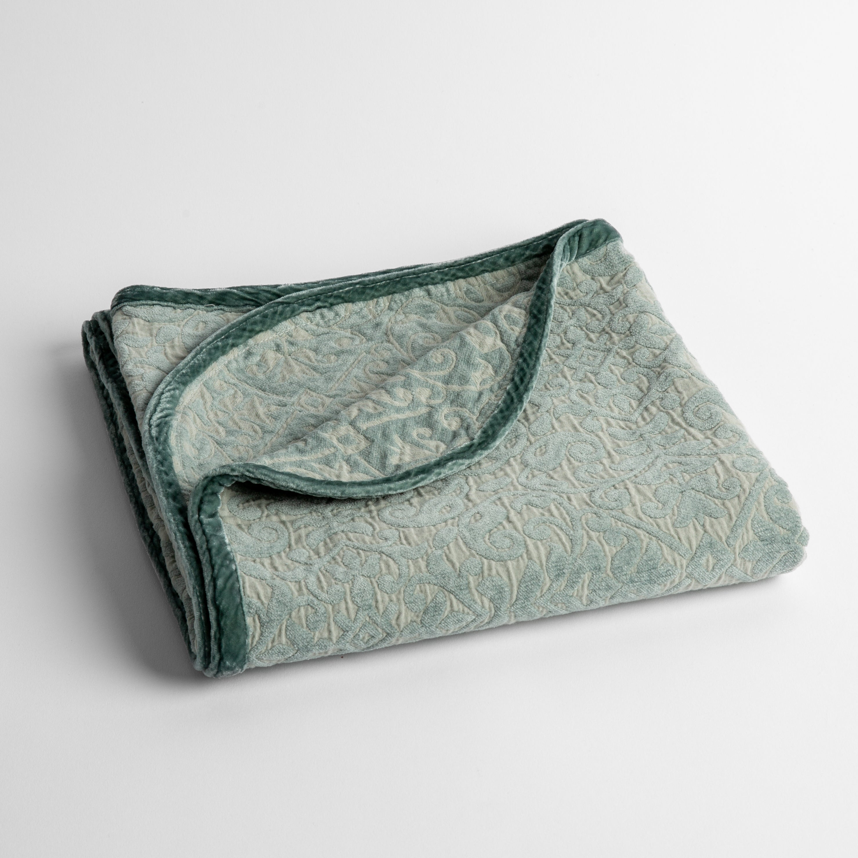 Eucalyptus: a folded cotton chenille baby blanket trimmed in silk velvet shot overhead at a slight angle against a white background. 