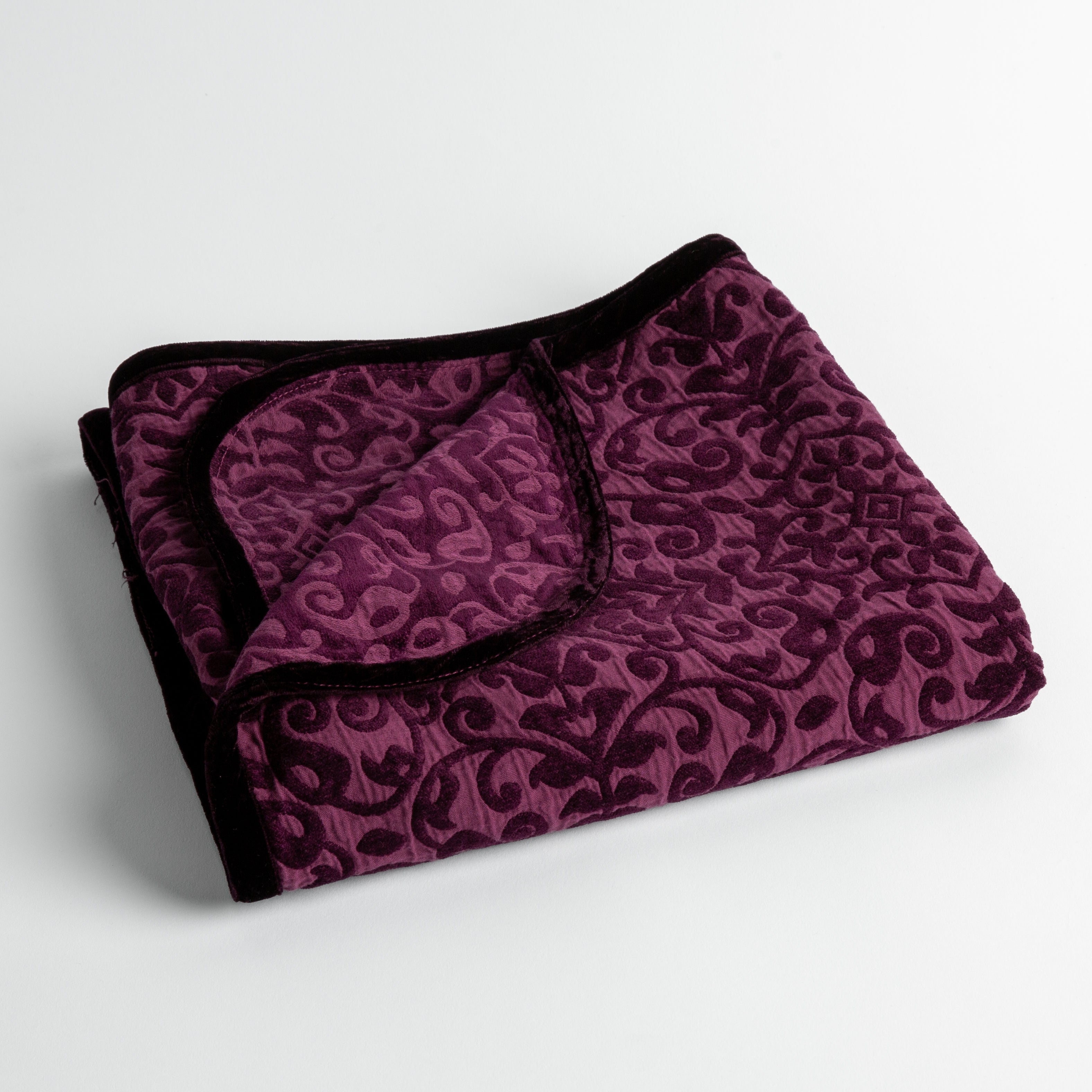 Fig: a folded cotton chenille baby blanket trimmed in silk velvet shot overhead at a slight angle against a white background. 