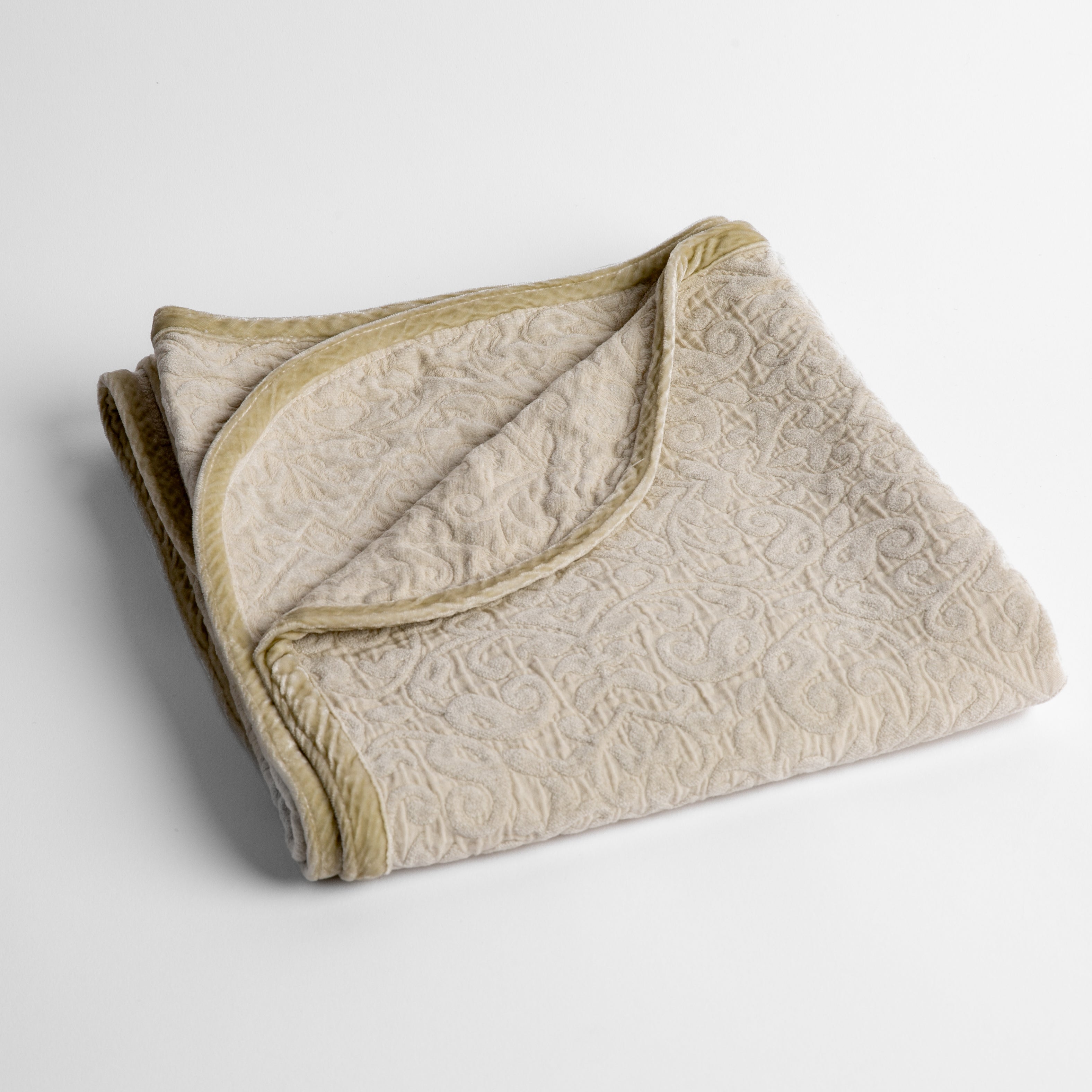 Parchment: a folded cotton chenille baby blanket trimmed in silk velvet shot overhead at a slight angle against a white background. 