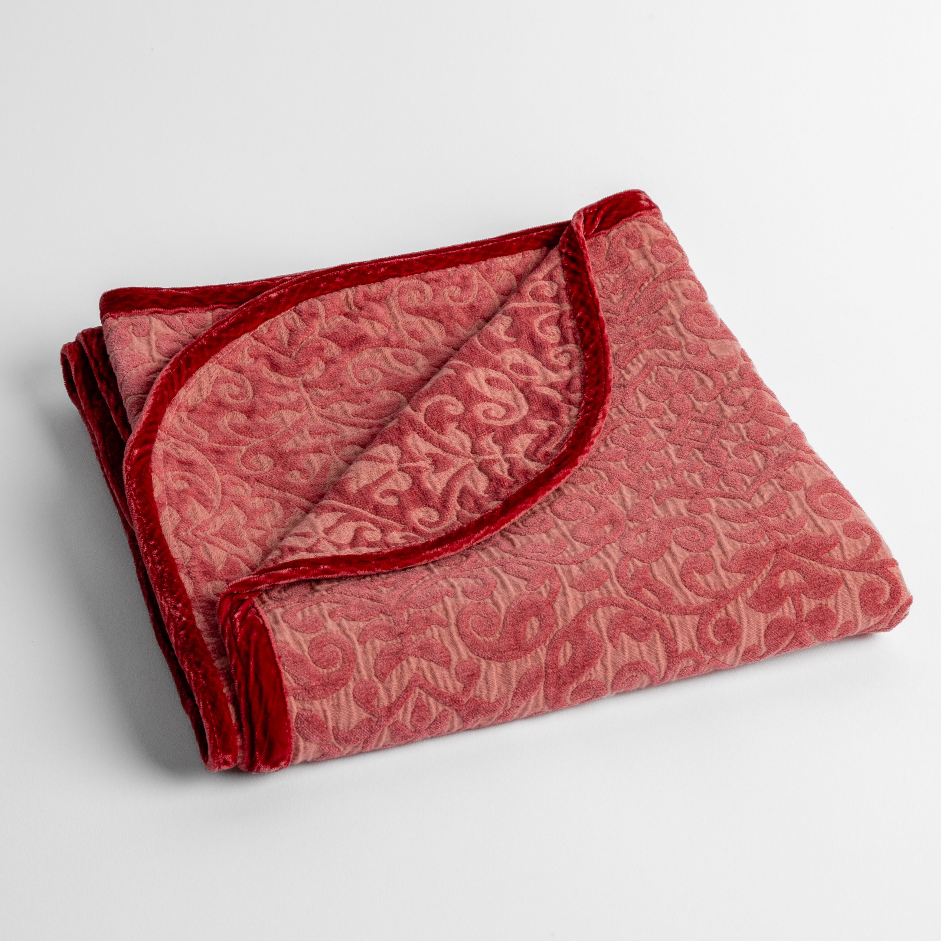 Poppy: a folded cotton chenille baby blanket trimmed in silk velvet shot overhead at a slight angle against a white background. 