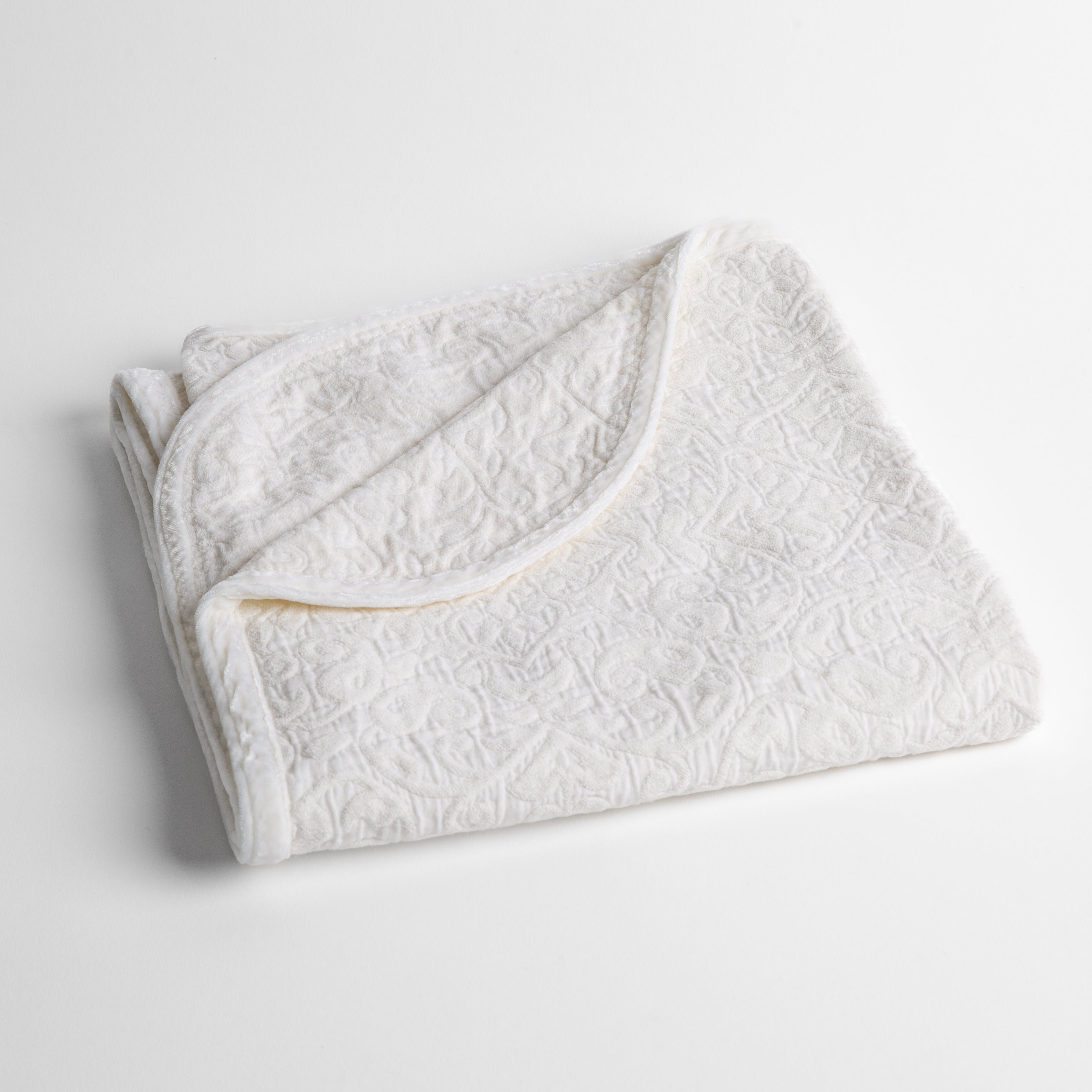 White: a folded cotton chenille baby blanket trimmed in silk velvet shot overhead at a slight angle against a white background. 