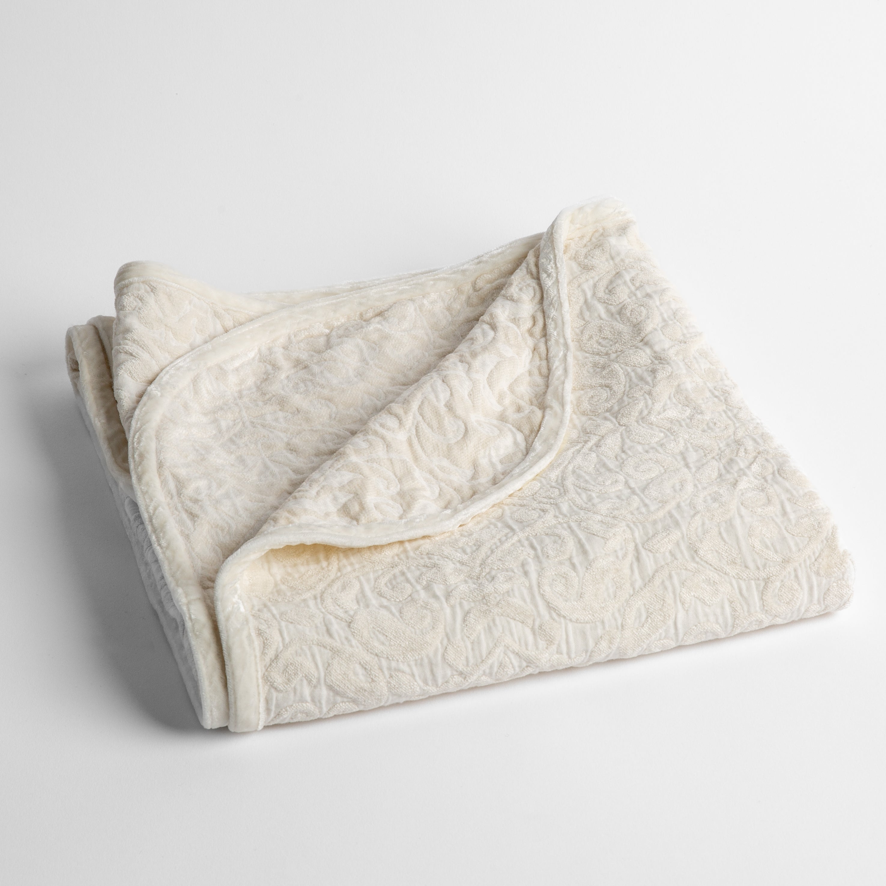 Winter White: a folded cotton chenille baby blanket trimmed in silk velvet shot overhead at a slight angle against a white background. 