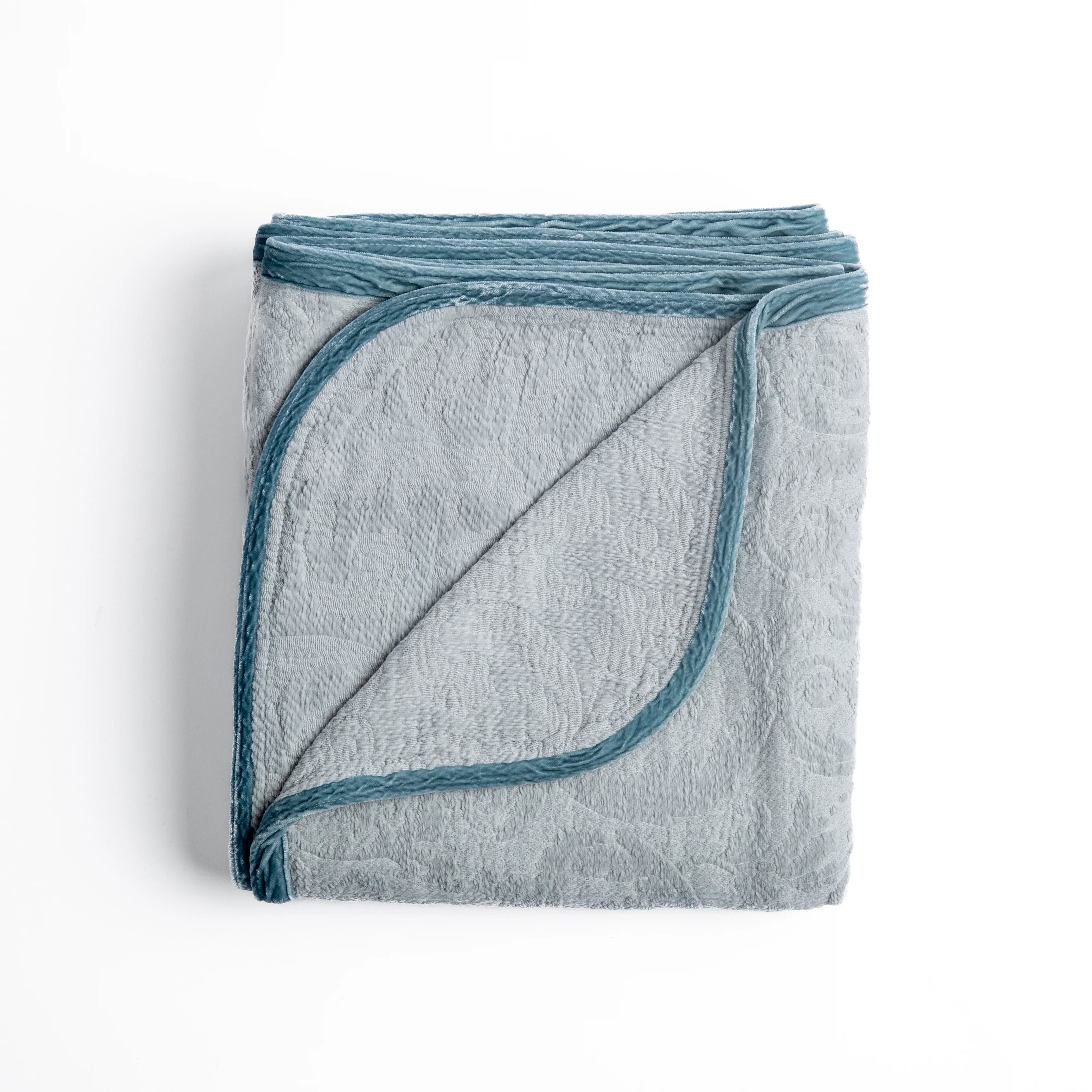 Cloud: folded organic cotton damask throw blanket shown with the corner folded down to show silk velvet trim detail — overhead against a plain white background. 