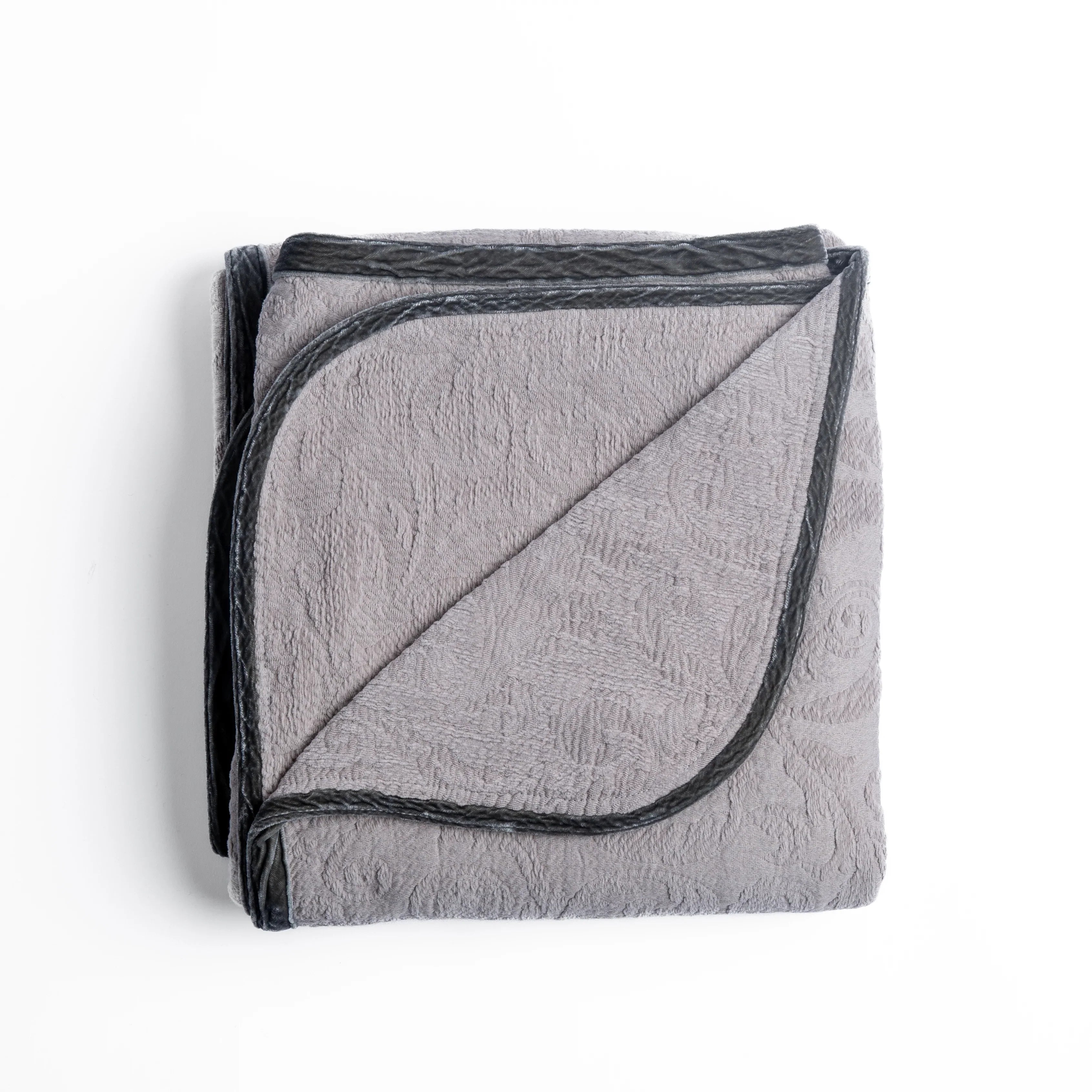 Fog: folded organic cotton damask throw blanket shown with the corner folded down to show silk velvet trim detail — overhead against a plain white background. 