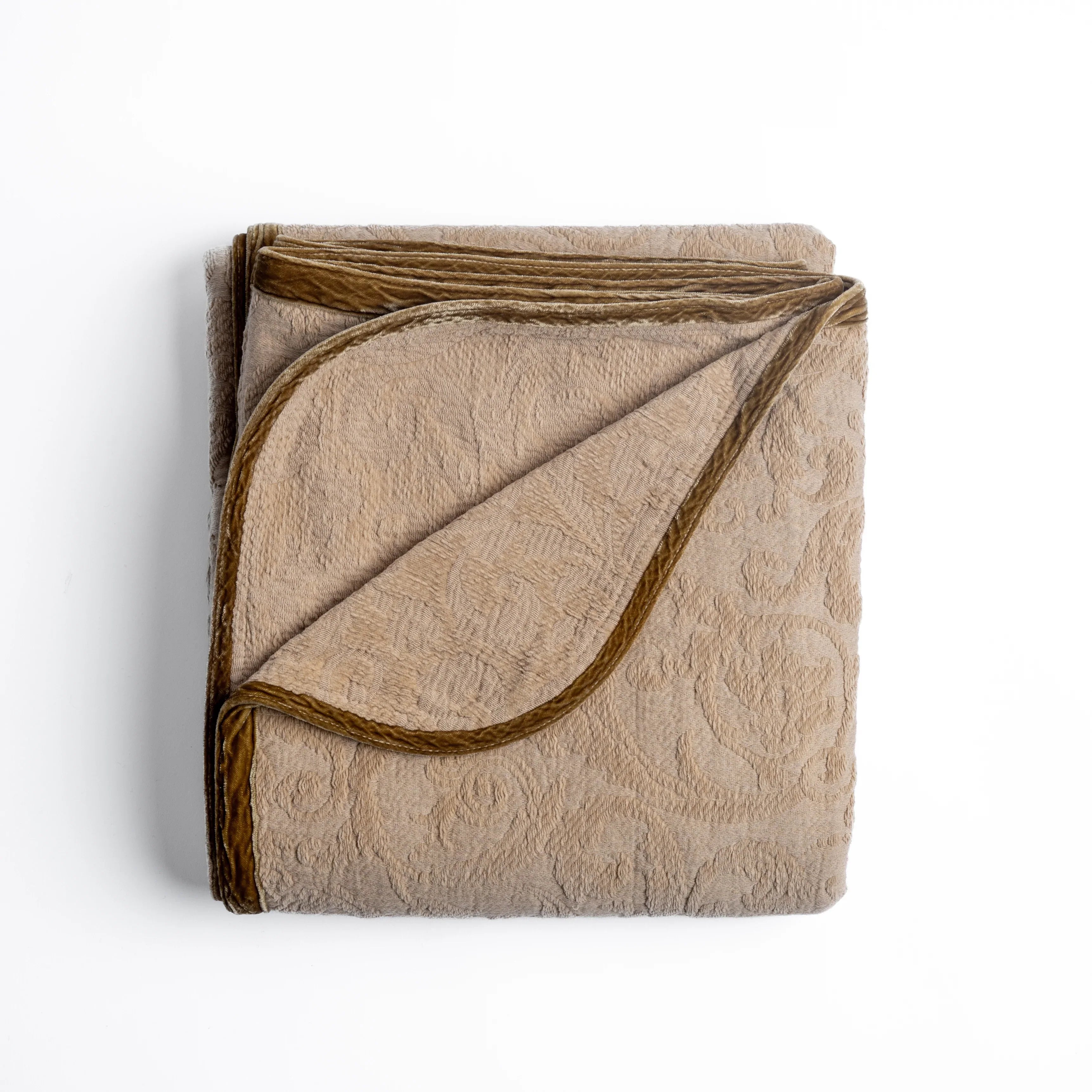 Honeycomb: folded organic cotton damask throw blanket shown with the corner folded down to show silk velvet trim detail — overhead against a plain white background. 