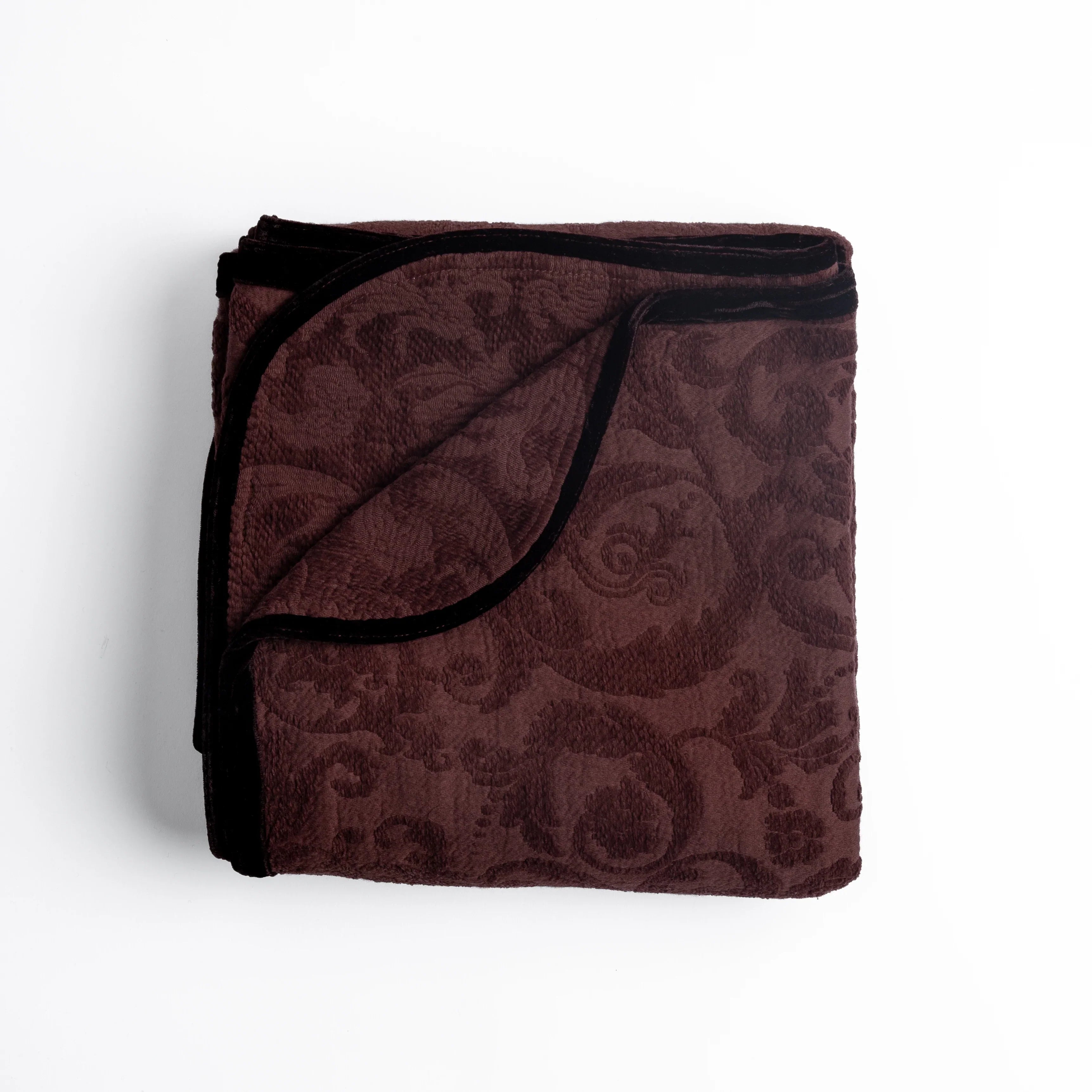 Mahogany: folded organic cotton damask throw blanket shown with the corner folded down to show silk velvet trim detail — overhead against a plain white background. 