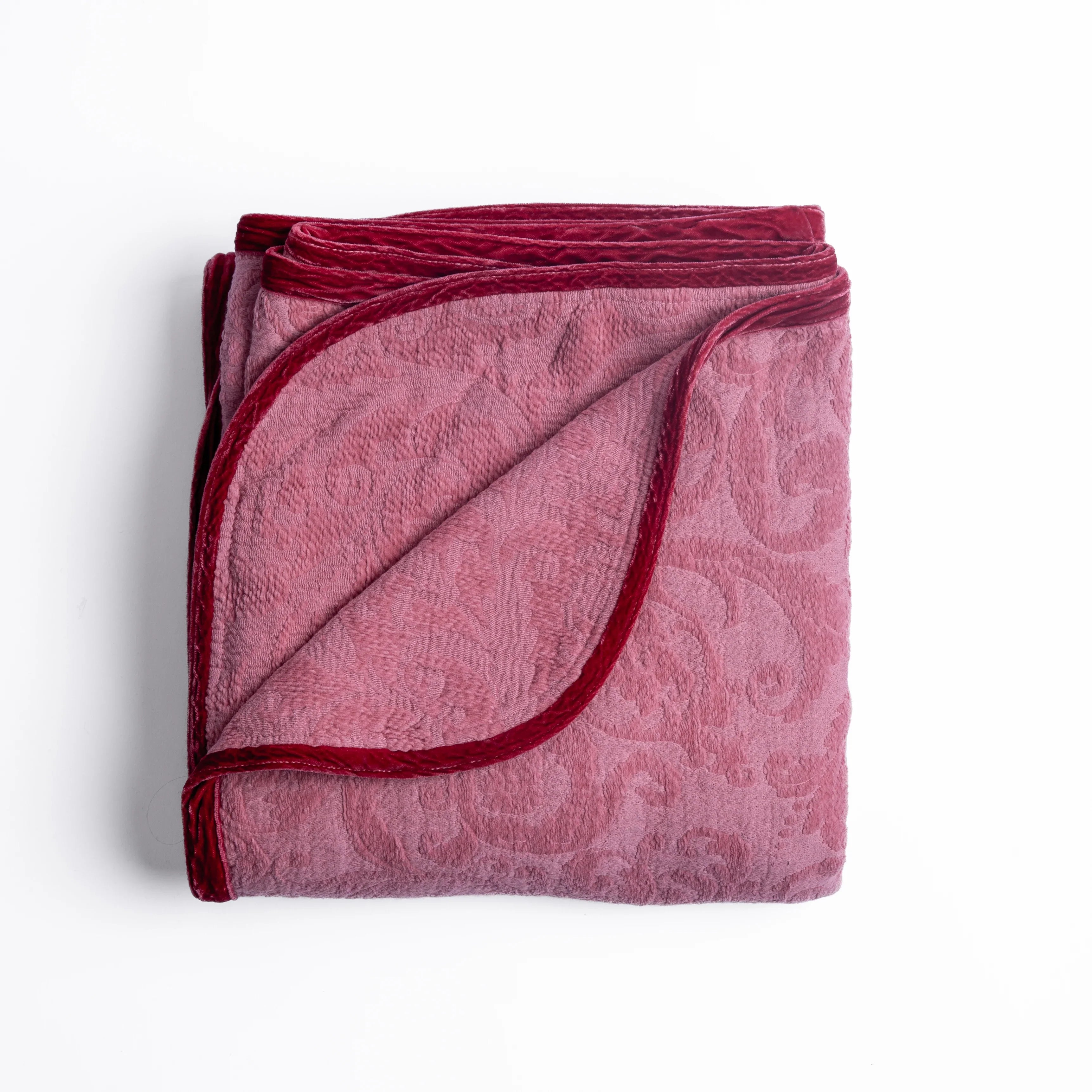Poppy: folded organic cotton damask throw blanket shown with the corner folded down to show silk velvet trim detail — overhead against a plain white background. 