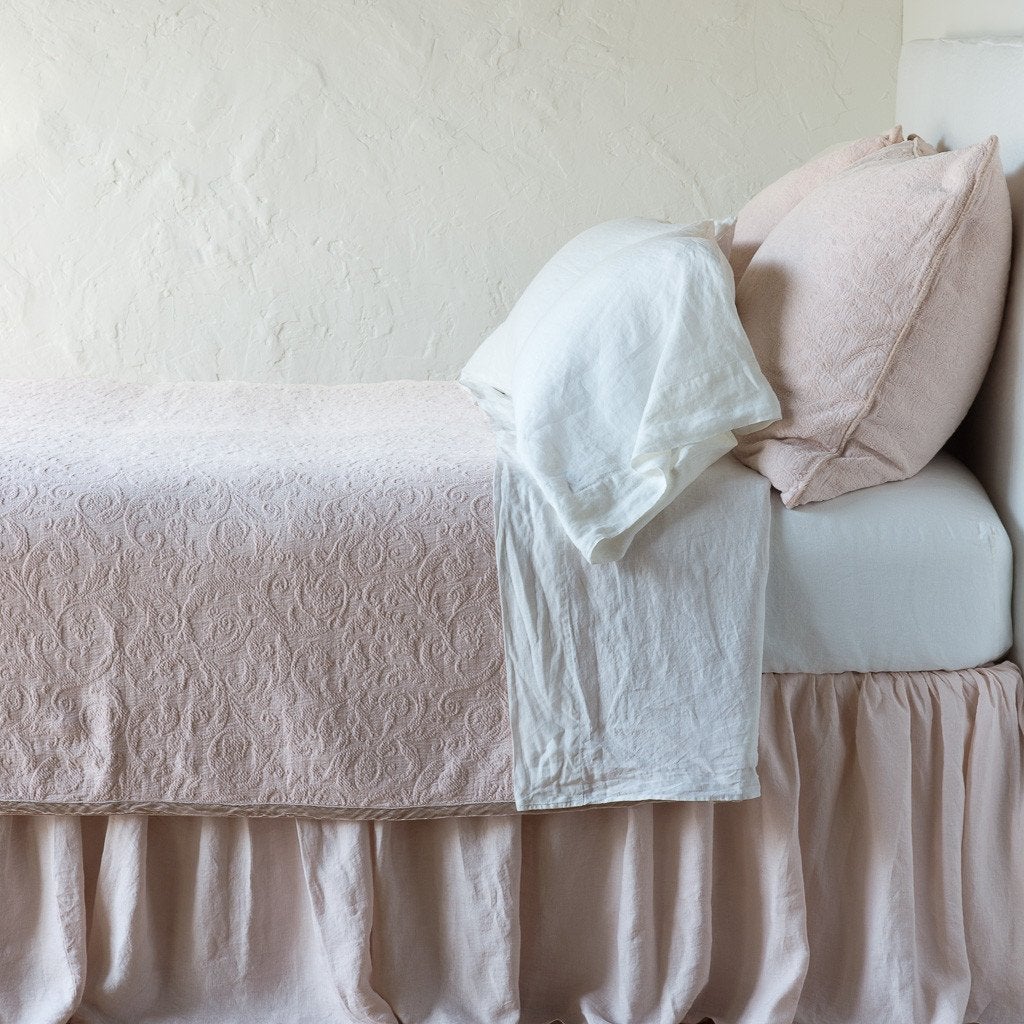 Pearl: The Adele coverlet in pearl, on a bed viewed from the side against a plain white wall. The bed is styled neatly with the coverlet folded back to reveal white sheets, bed skirt and pillows.