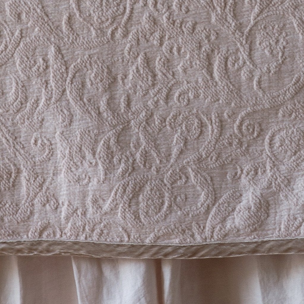 Pearl: Close up of the Adele coverlet in pearl, highlighting the detail of the cotton damask and the silk velvet edging trim. A white bed skirt peeks out at the bottom of the shot.