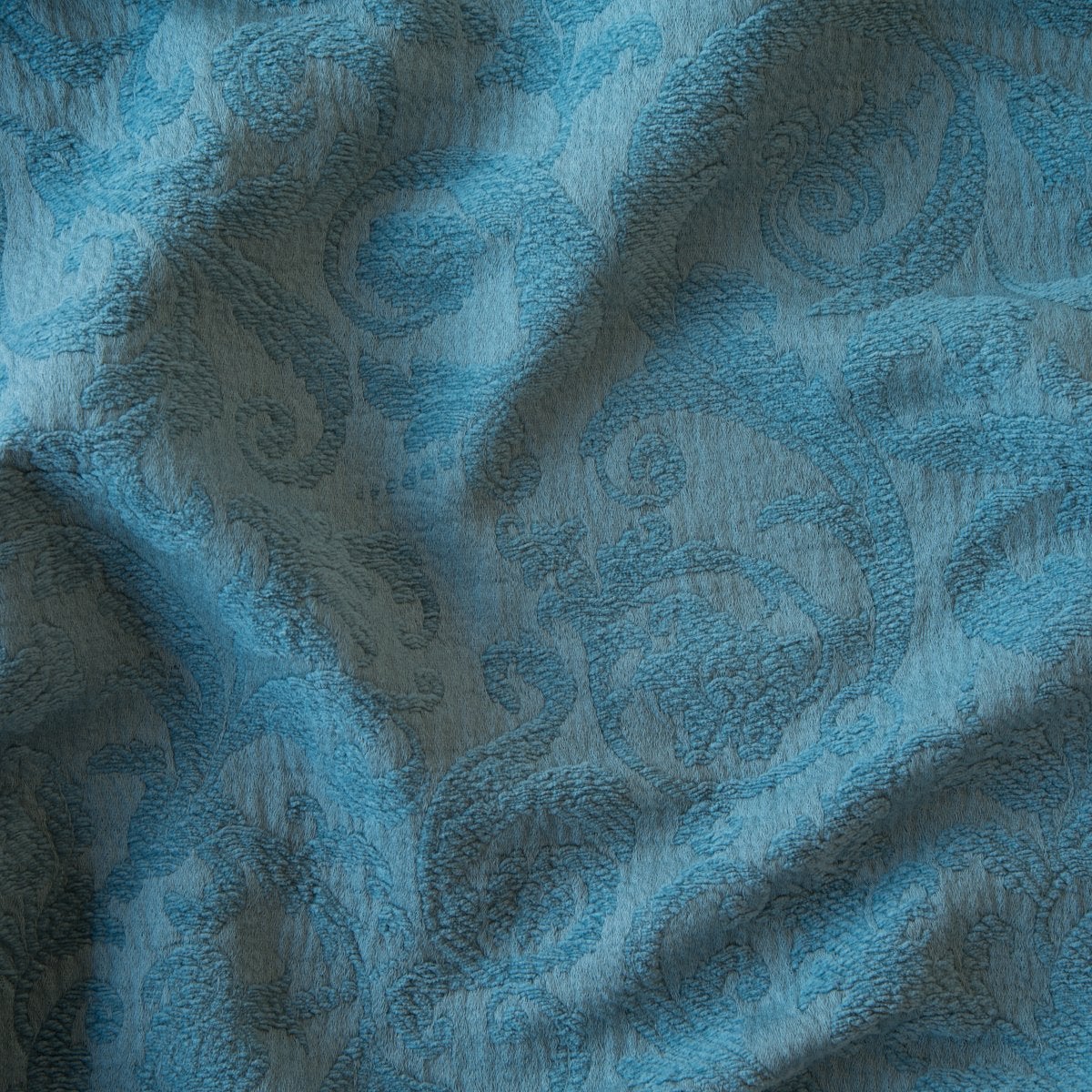 Cenote: A close up of Adele fabric in cenote, a vibrant, ocean-inspired blue-green. The fabric is rumpled to show the cotton damask texture.