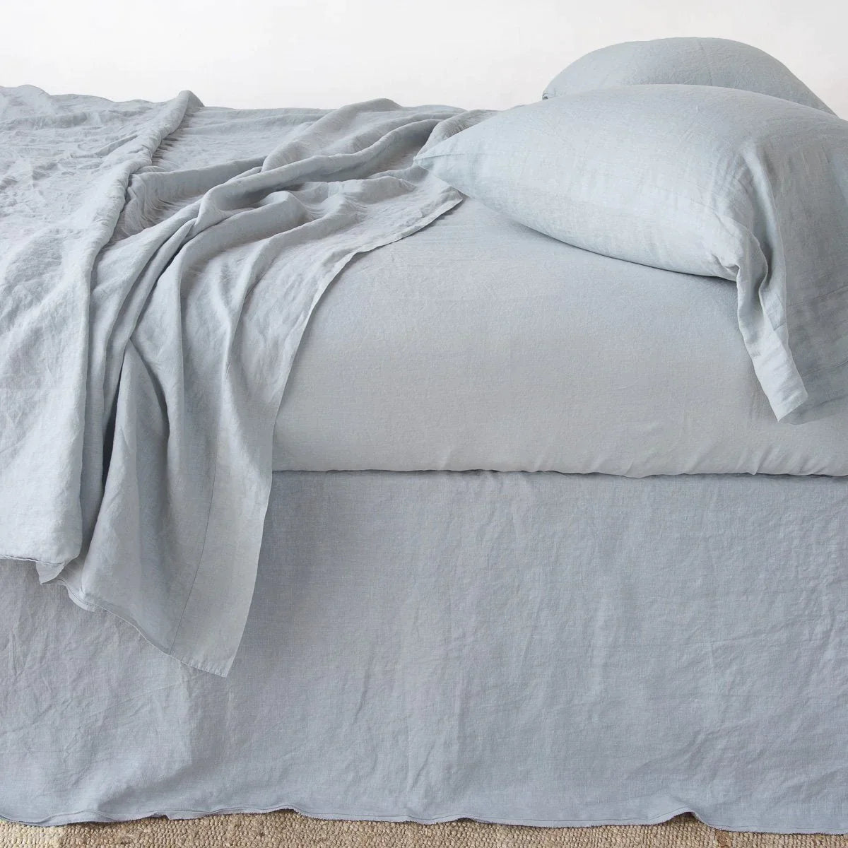 Mineral: Austin bed skirt in mineral shown from the side on a bed with monochromatic sheeting, highlighting its tailored, ungathered style.