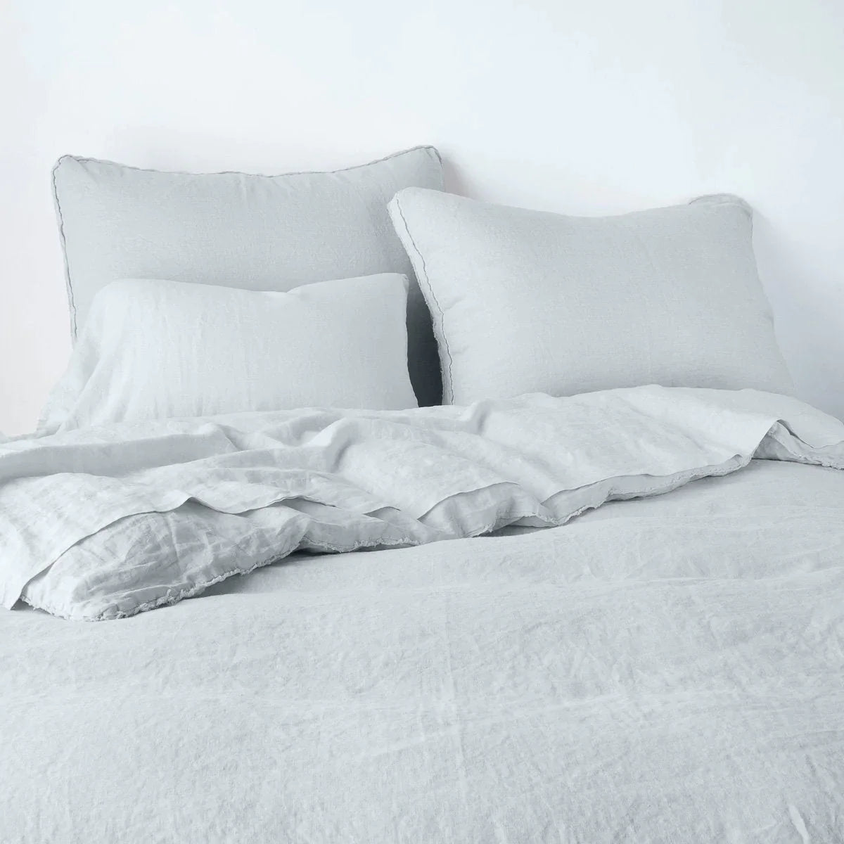 Cloud: Midweight linen shams shown from foot of bed, leaning against a plain background with monochromatic bedding. 