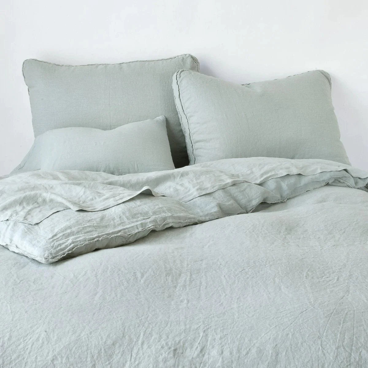 Eucalyptus: Midweight linen shams shown from foot of bed, leaning against a plain background with monochromatic bedding. 