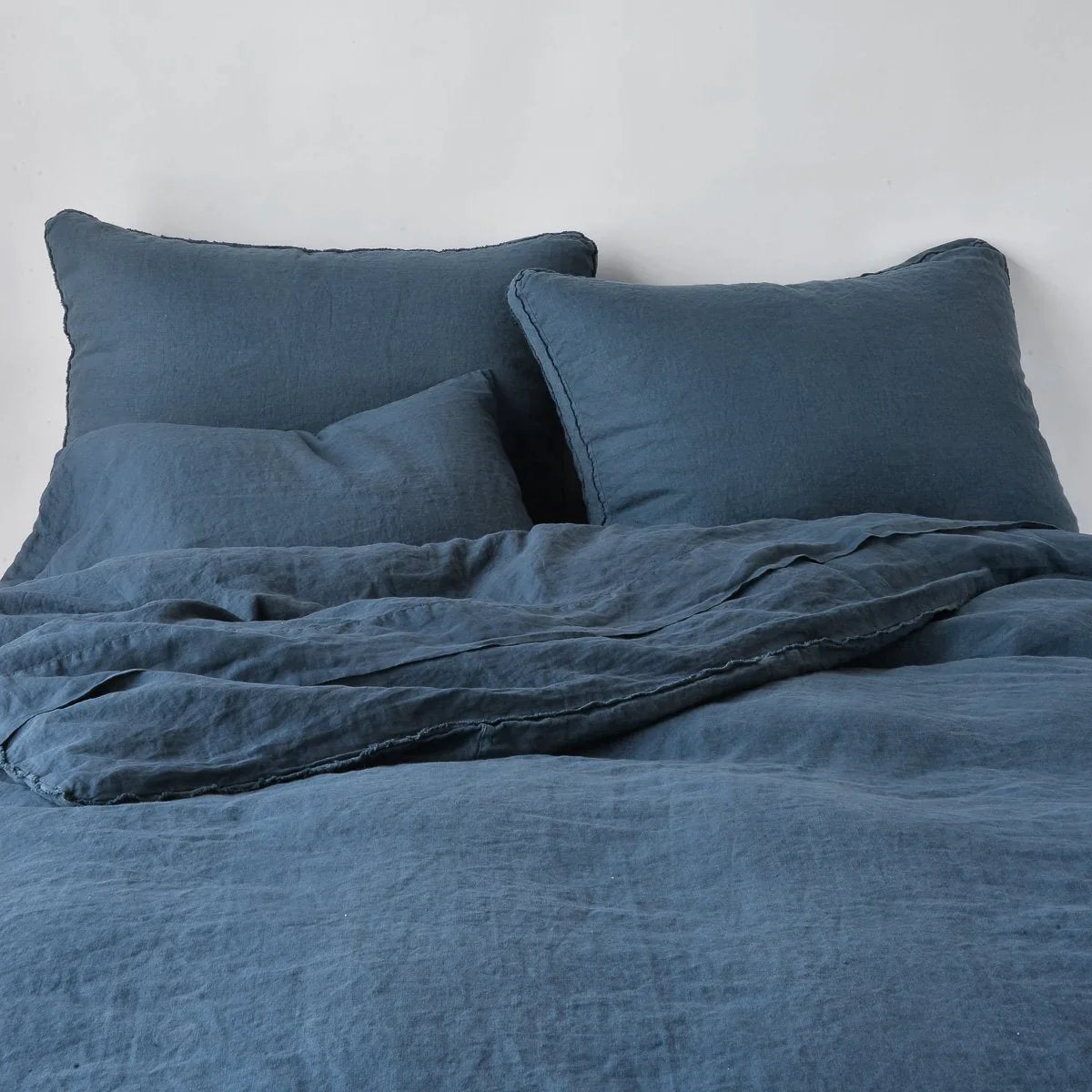 Midnight: Midweight linen shams shown from foot of bed, leaning against a plain background with monochromatic bedding. 