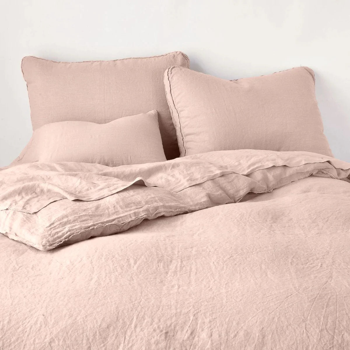 Rouge: Midweight linen shams shown from foot of bed, leaning against a plain background with monochromatic bedding. 