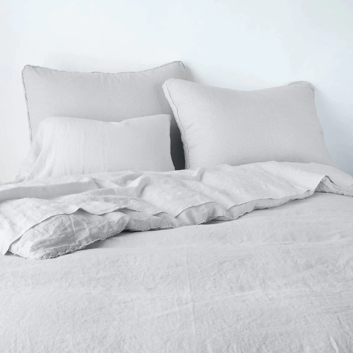 Sterling: Midweight linen shams shown from foot of bed, leaning against a plain background with monochromatic bedding. 