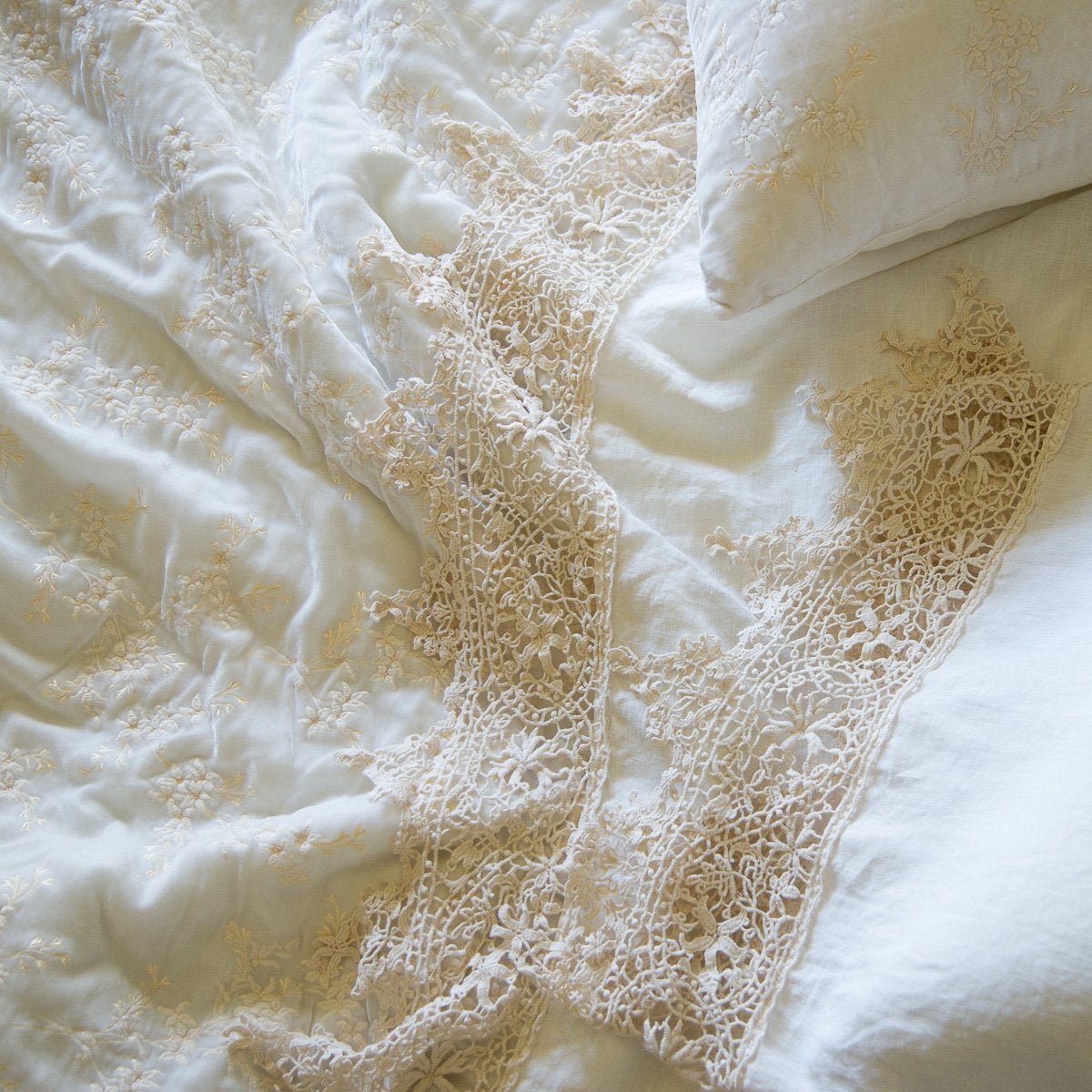: Close up of a Frida flat sheet and pillowcase, layered over embroidered silk velvet, all in winter white - overhead view.