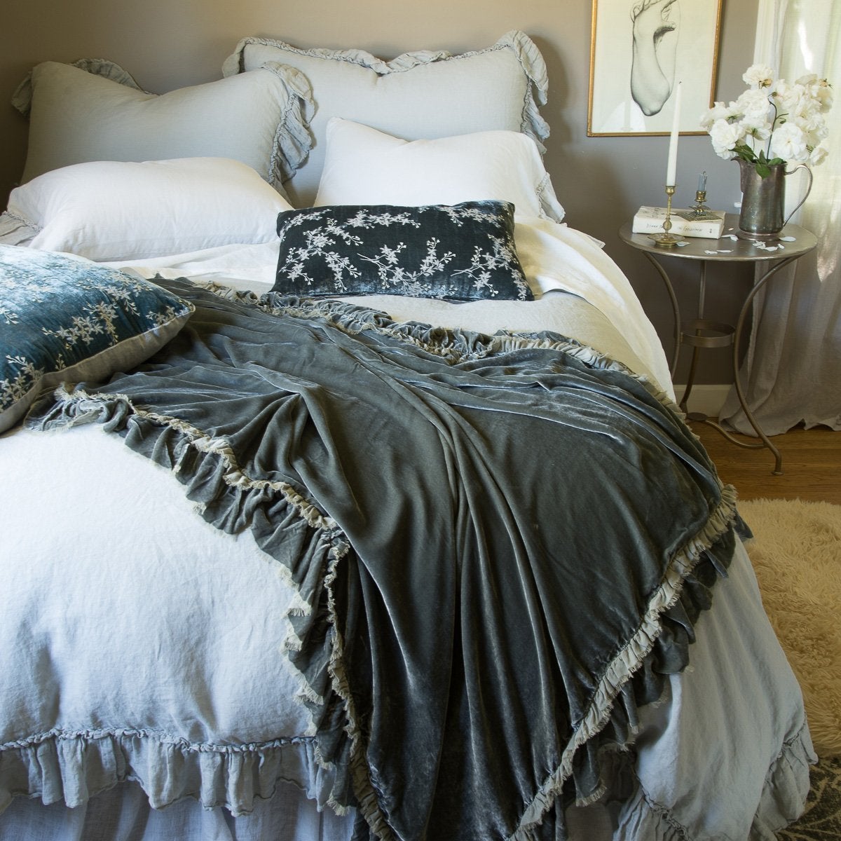 : Linen Whisper bed duvet cover in mineral, layered with a matching bed skirt and richly colored silk velvet accessory pieces - end of bed view.