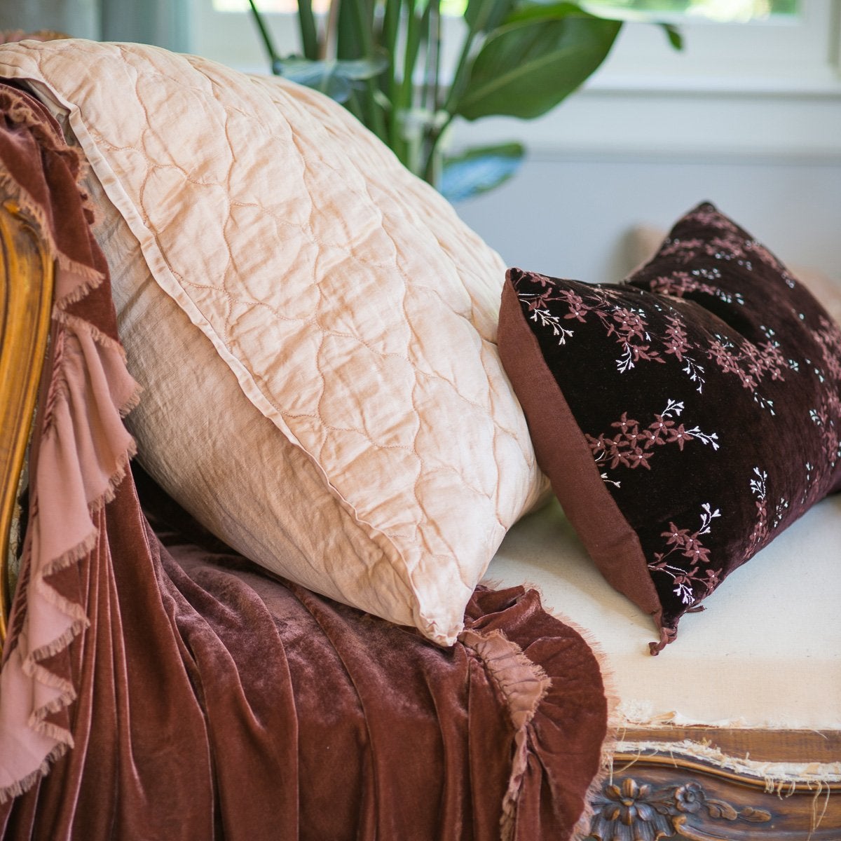 [allvariants]: Luna coverlet on a fig bed, with mixed textures of cotton velvet, embroidered linen, tassled silk charmeuse, and silk velvet. Deep blue throw pillows and dark blue background create a moody vibe.