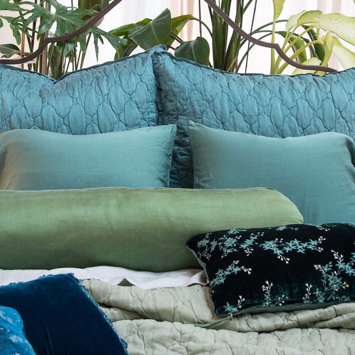 : Luna shams in cenote with sleeping and throw pillows in green and blue tones, with big leafy green plants in the background - close-up head on view.
