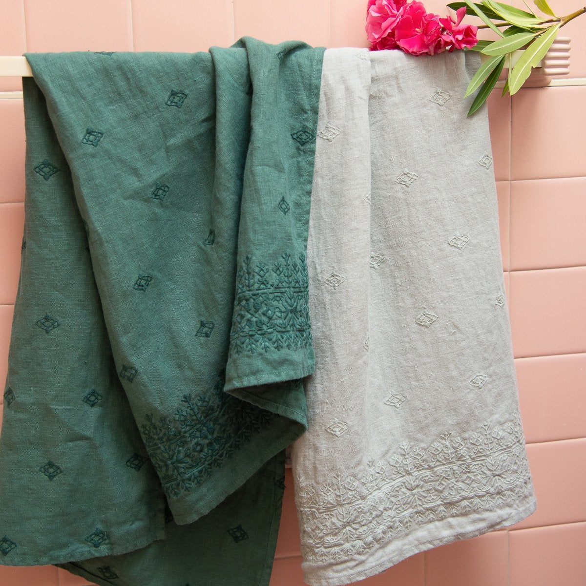 : Ines guest towels in jade and eucalyptus, rumpled on a towel bar against a pink tiled wall.