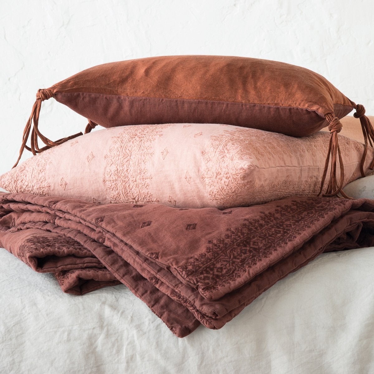 : Ines throw blanket in mahogany, stacked rouge Ines and mahogany charmeuse throw pillows on a light backgroud - side view.