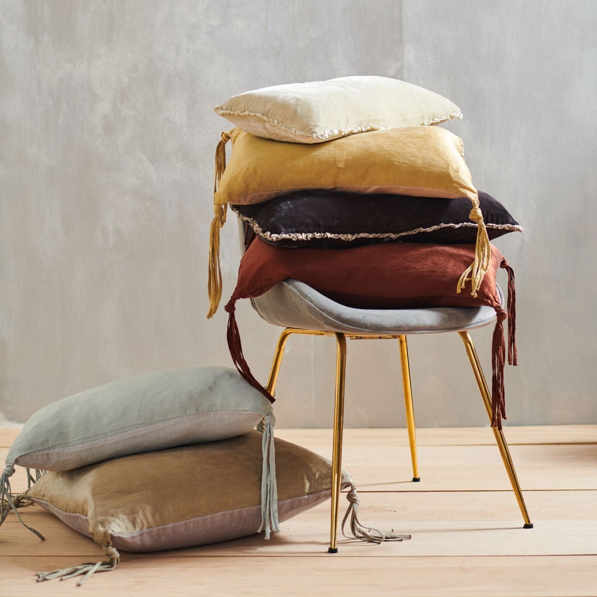 : Carmen lumbar pillow stacked on a light grey chair with silk velvet and silk charmeuse throw pillows  in earthy, gold, brown, and neutral tones.