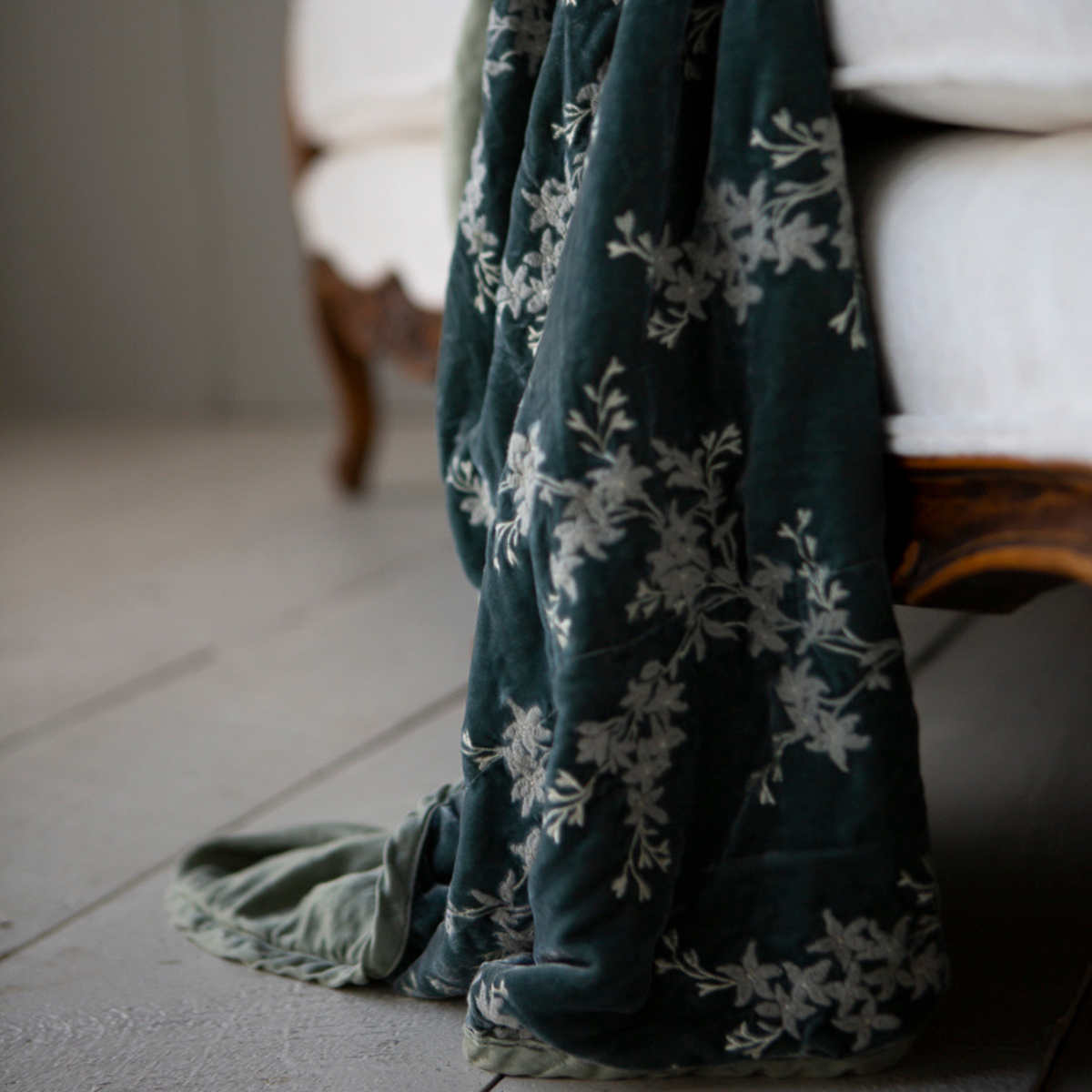 : close up of embroidered silk velvet with charmeuse trim and back, hanging off of the edge of a white couch sofa with wood detail. 