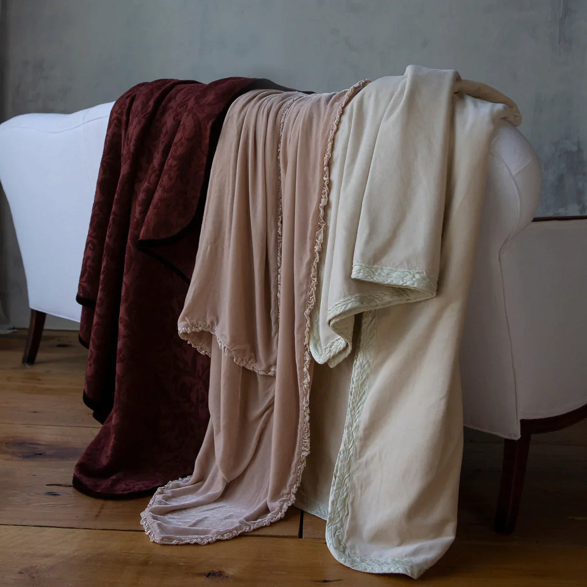 : three throw blankets draped over the back of a white sofa. The adele throw blanket is on the far left in Mahogany. 