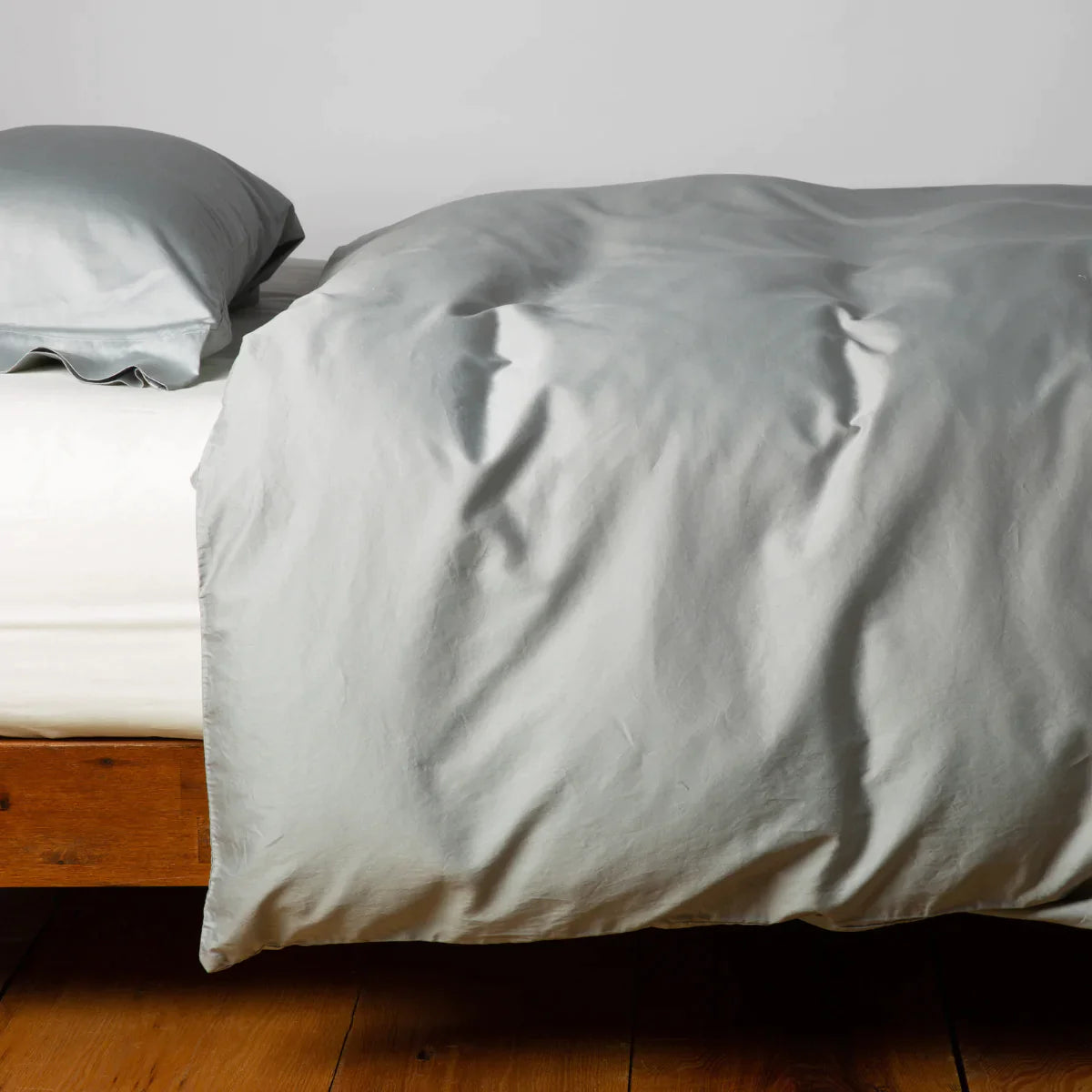 [allvariants]: Cotton sateen duvet cover in mineral with matching sleeping pillow on white sheeting - side view.