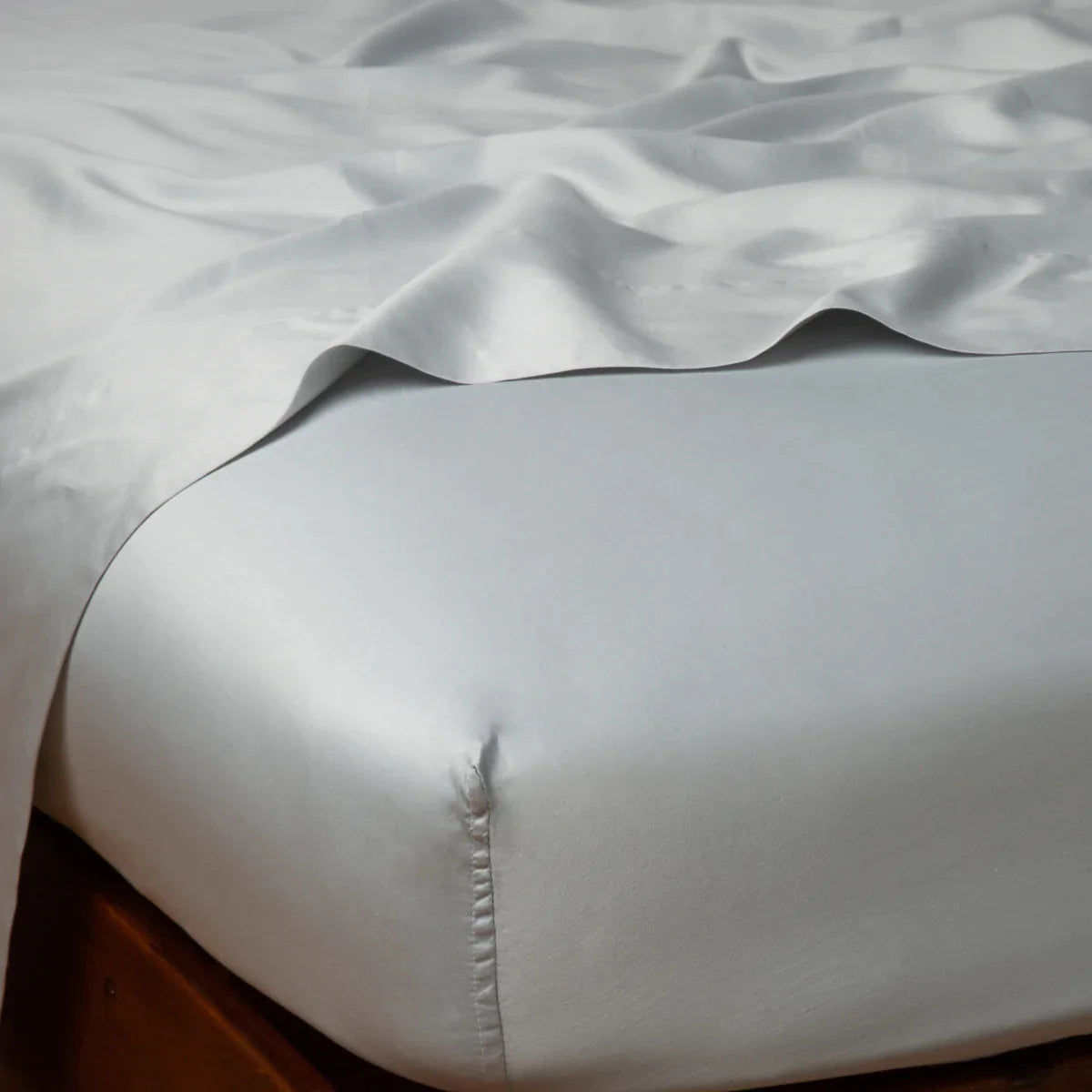 Cloud: Cotton sateen flat sheet draped over matching fitted sheet. Shown from the top corner, the flat sheet is rumpled, highlighting the shine of the fabric.