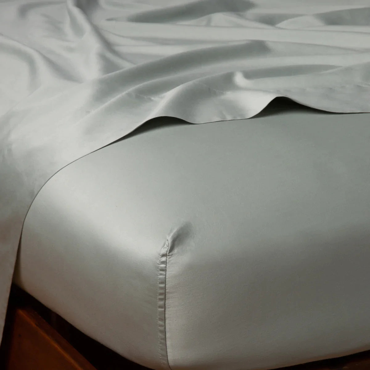Eucalyptus: Cotton sateen flat sheet draped over matching fitted sheet. Shown from the top corner, the flat sheet is rumpled, highlighting the shine of the fabric.