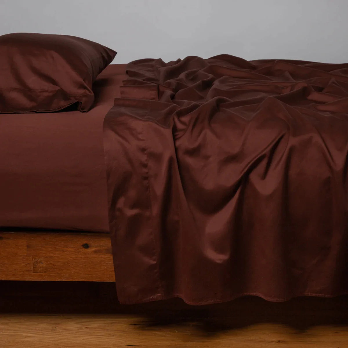 Mahogany: Cotton sateen flat sheet, shown with matching fitted sheet and sleeping pillow - side view.